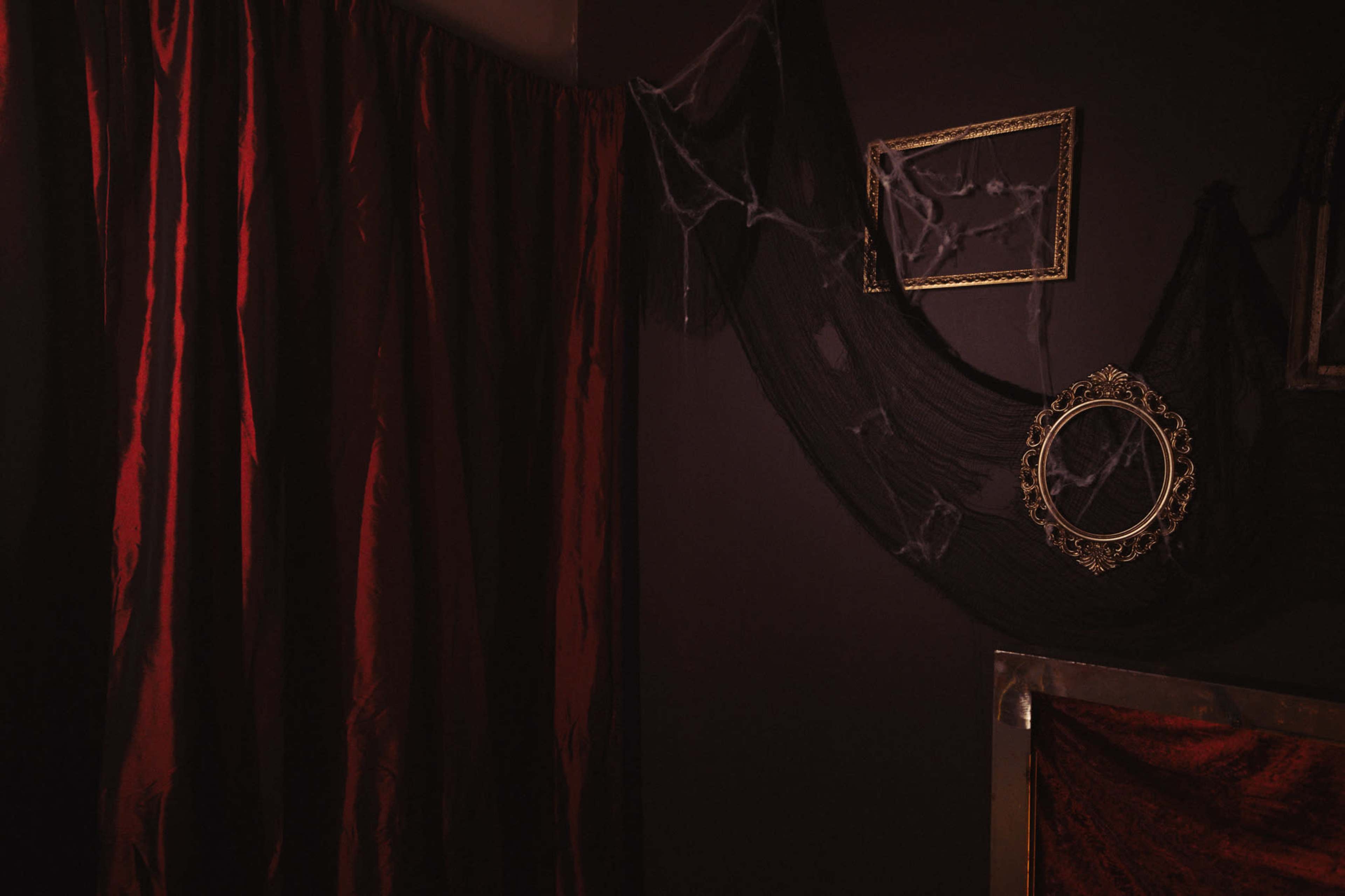 The image features a dimly lit room with red curtains, a cobweb-draped mirror, and dark walls.