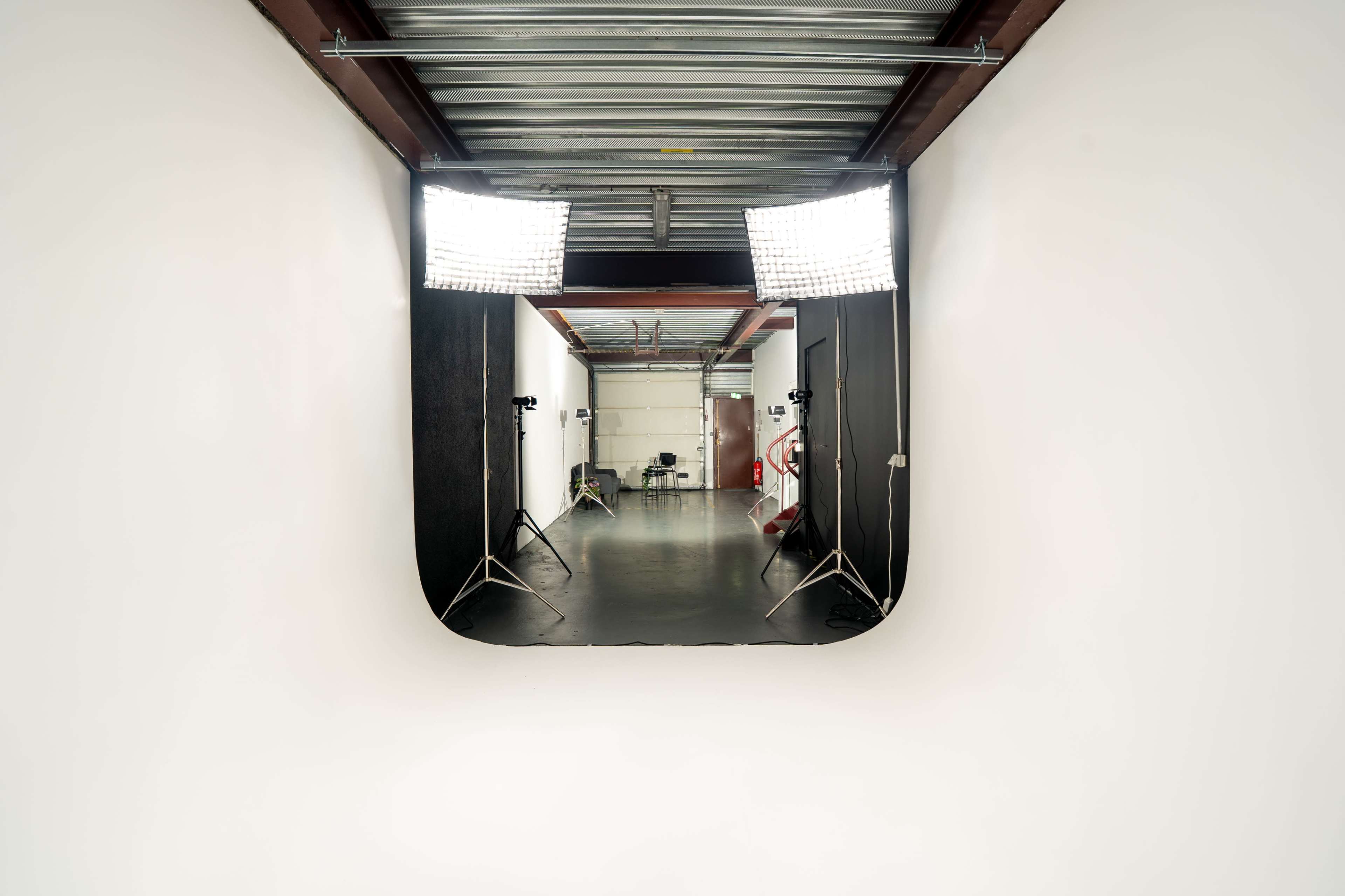 The image shows a well-lit studio space with softbox lights positioned at both sides of a backdrop in a hallway.