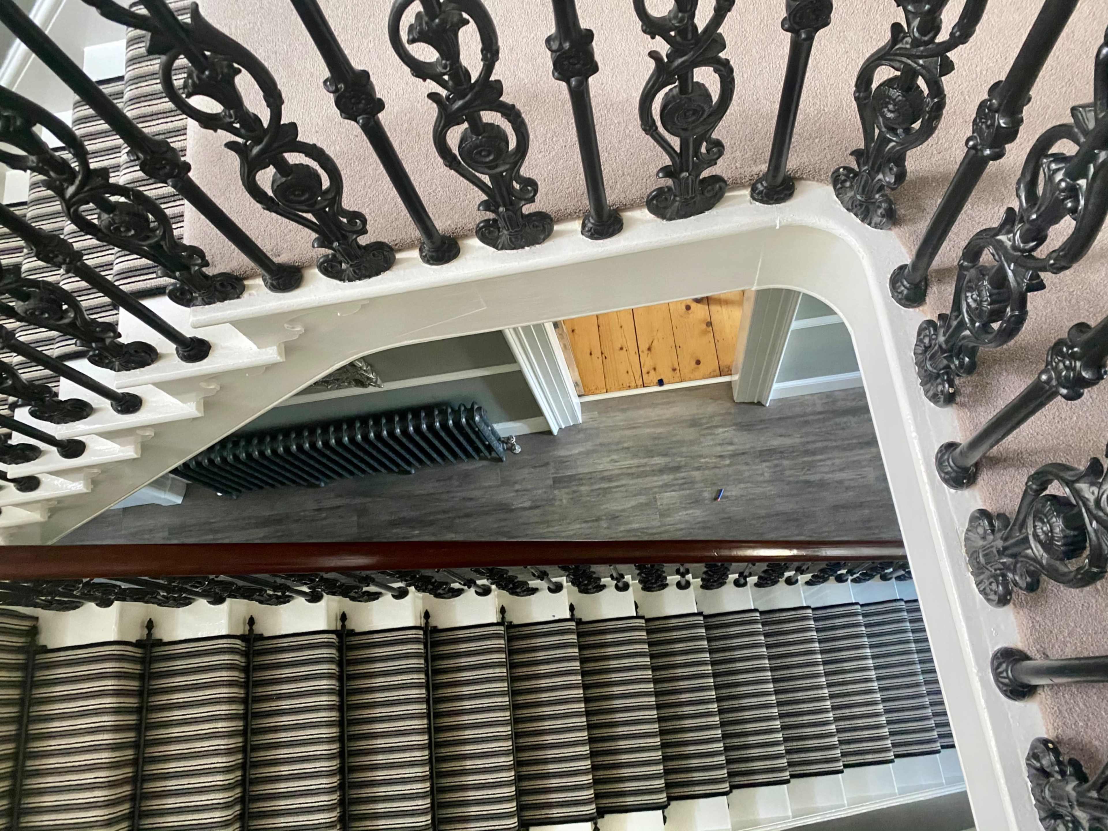 A view of a staircase with ornate iron railings and a carpeted stairway leading down to a hallway with wooden flooring.