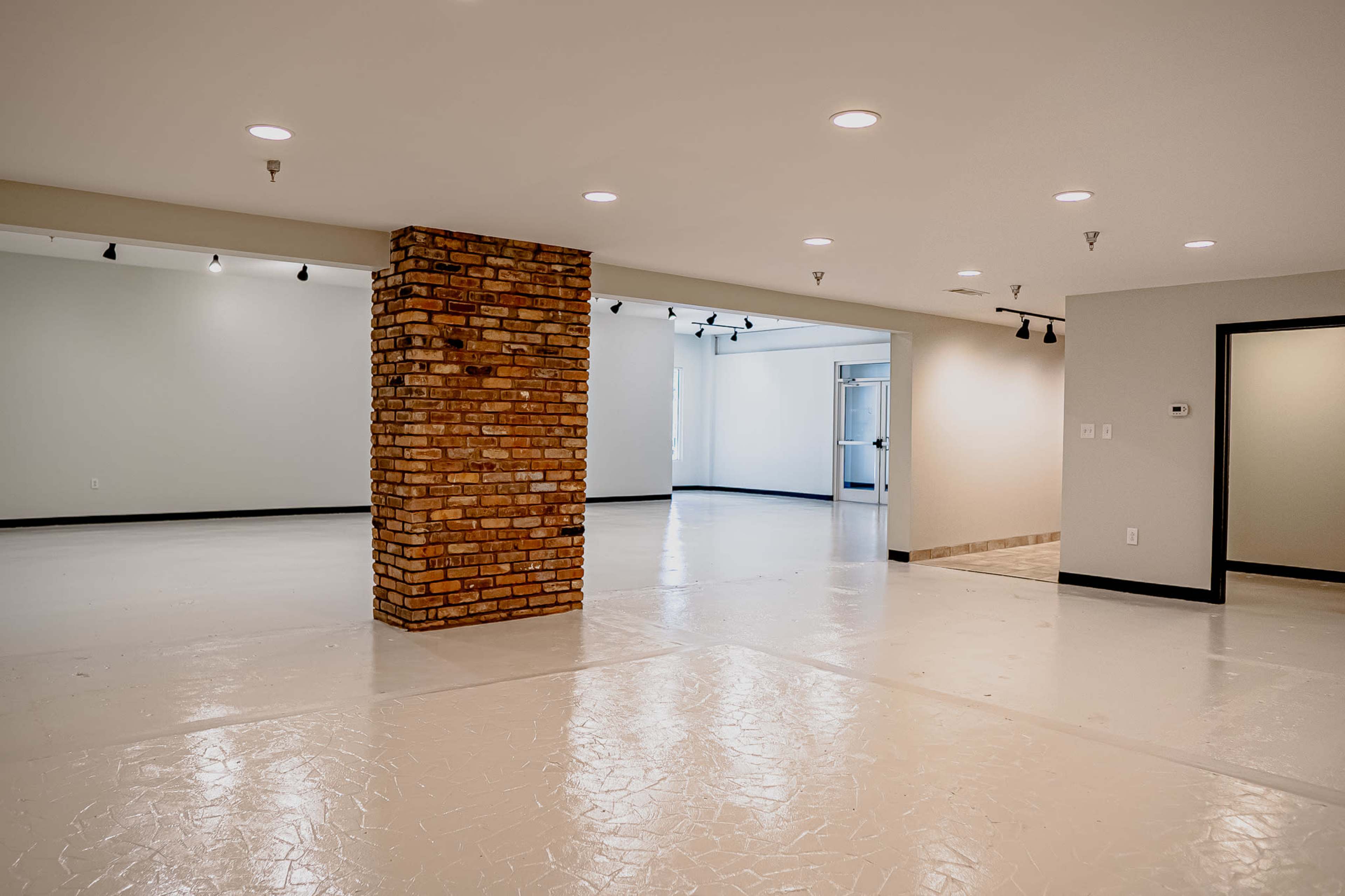 A spacious, empty interior room with polished white flooring and a central exposed brick column.