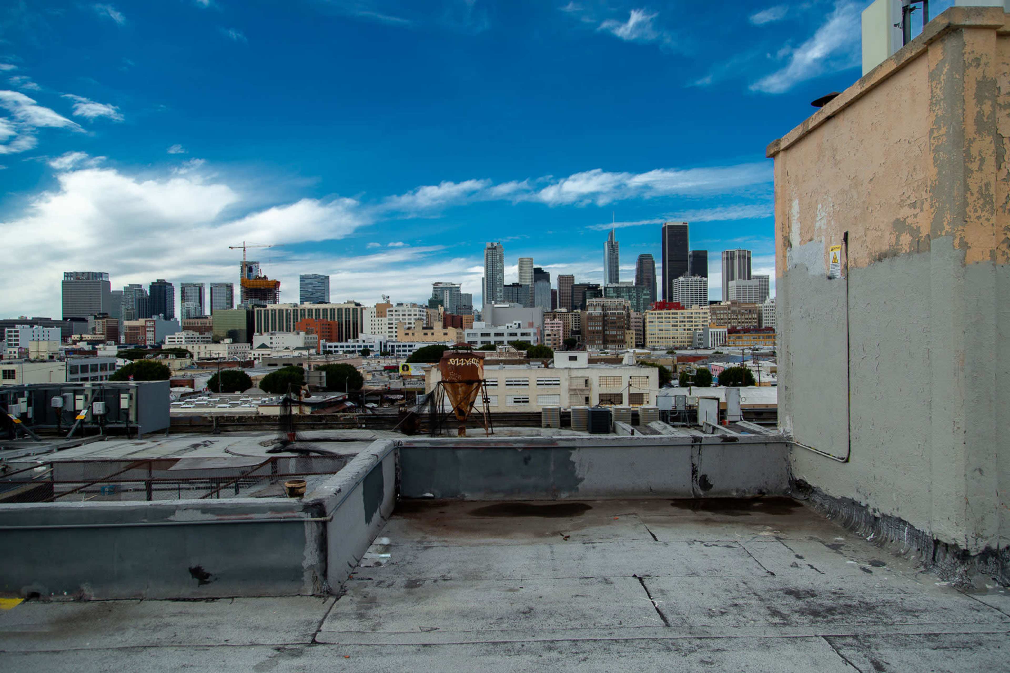 The image shows a rooftop overlooking a city skyline with modern buildings and a clear blue sky.