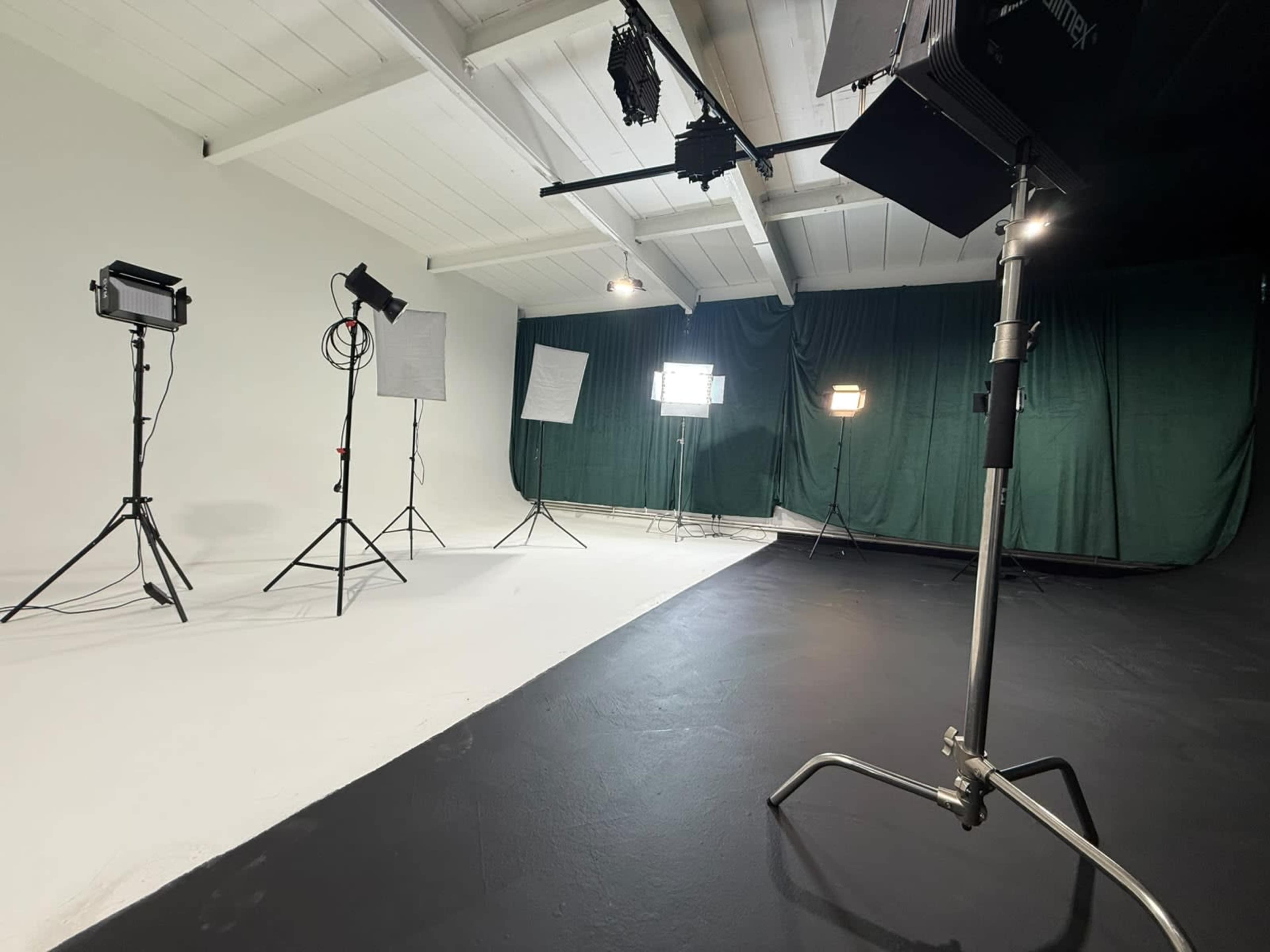 The image shows a photography studio with various lighting equipment set up on a black floor and a green backdrop.