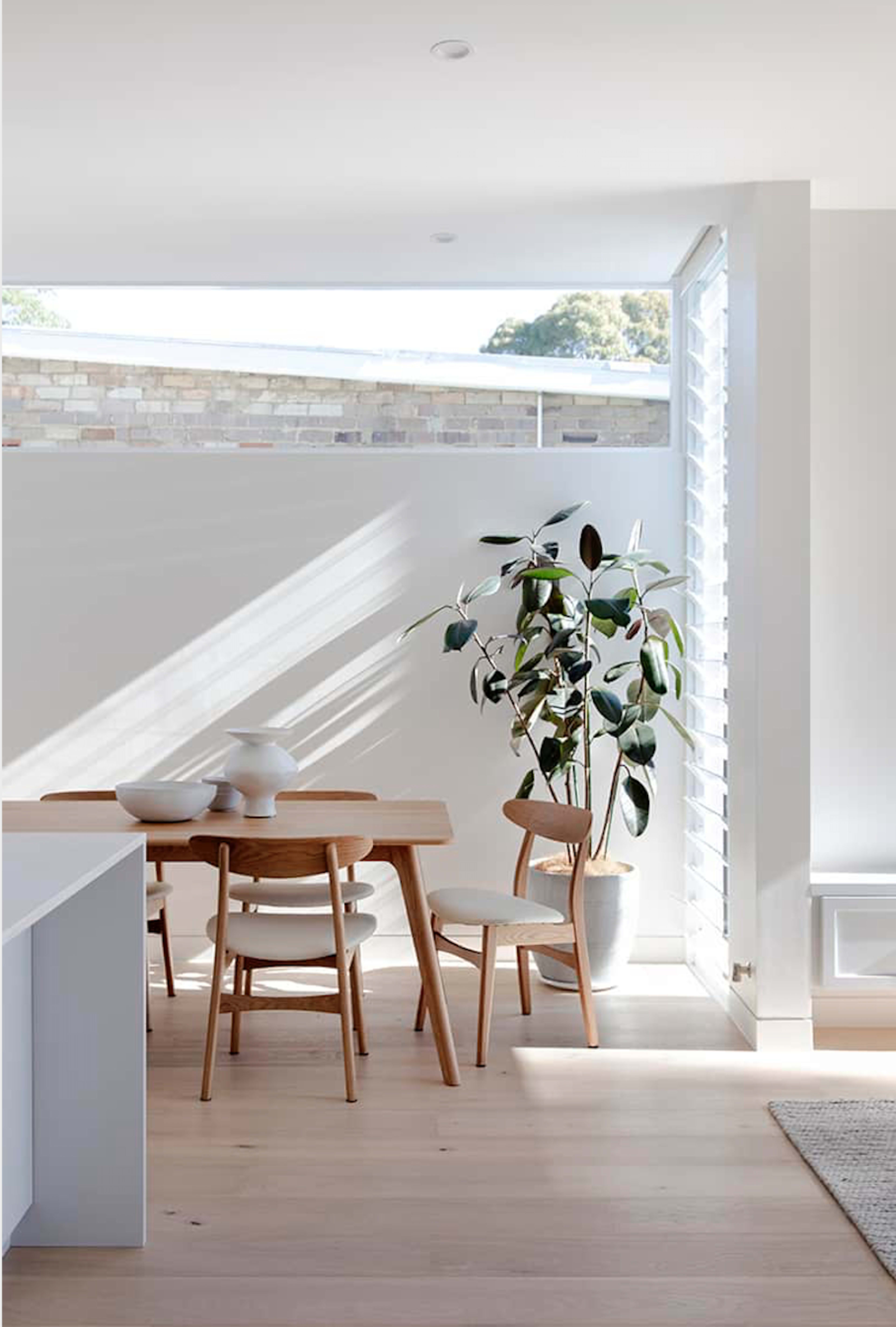 A wooden dining table with three chairs and a potted plant is positioned near a window that lets in natural light.