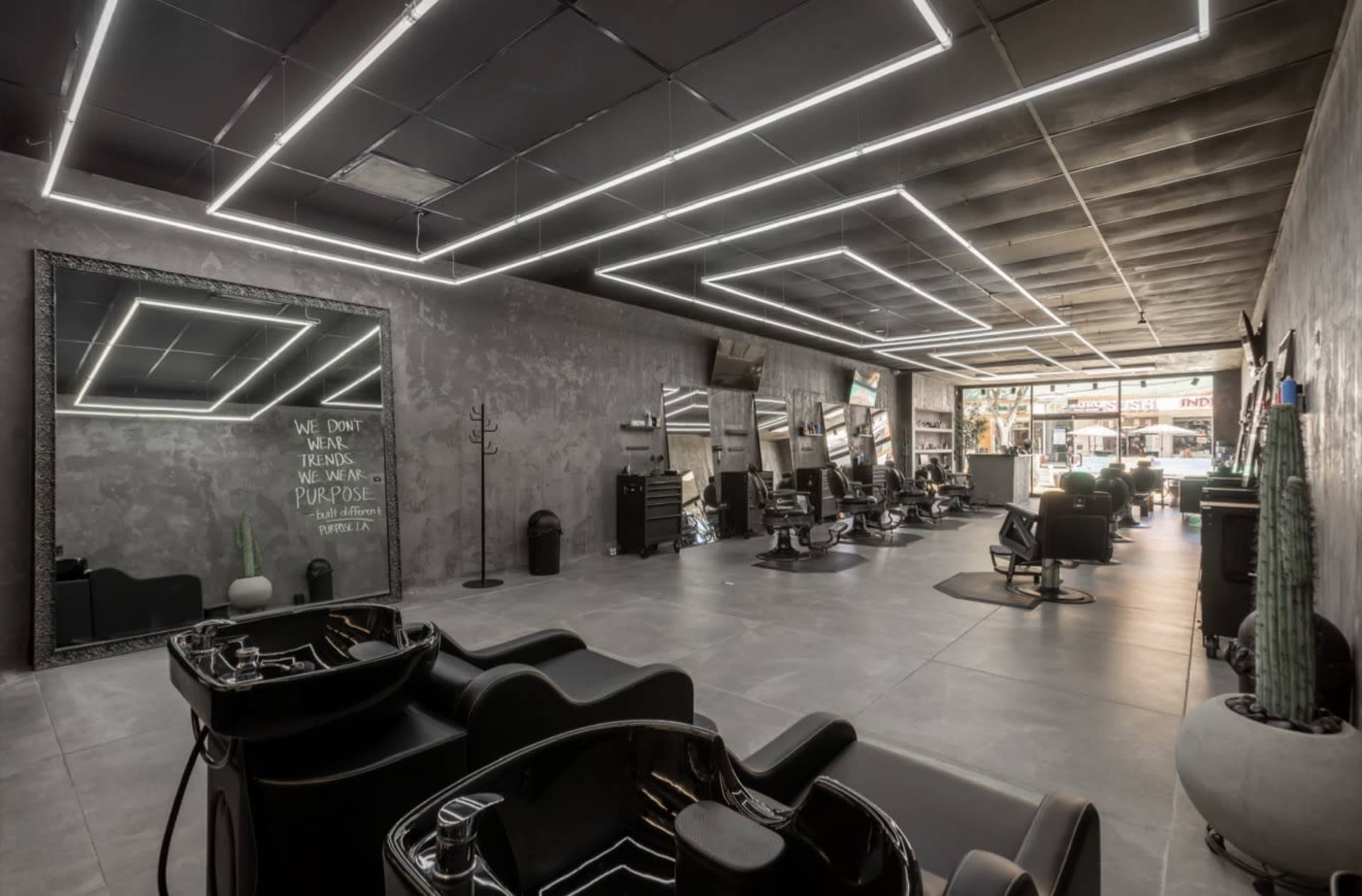 The image shows a modern hair salon featuring black salon chairs, mirrors, and contemporary lighting fixtures against a gray wall.