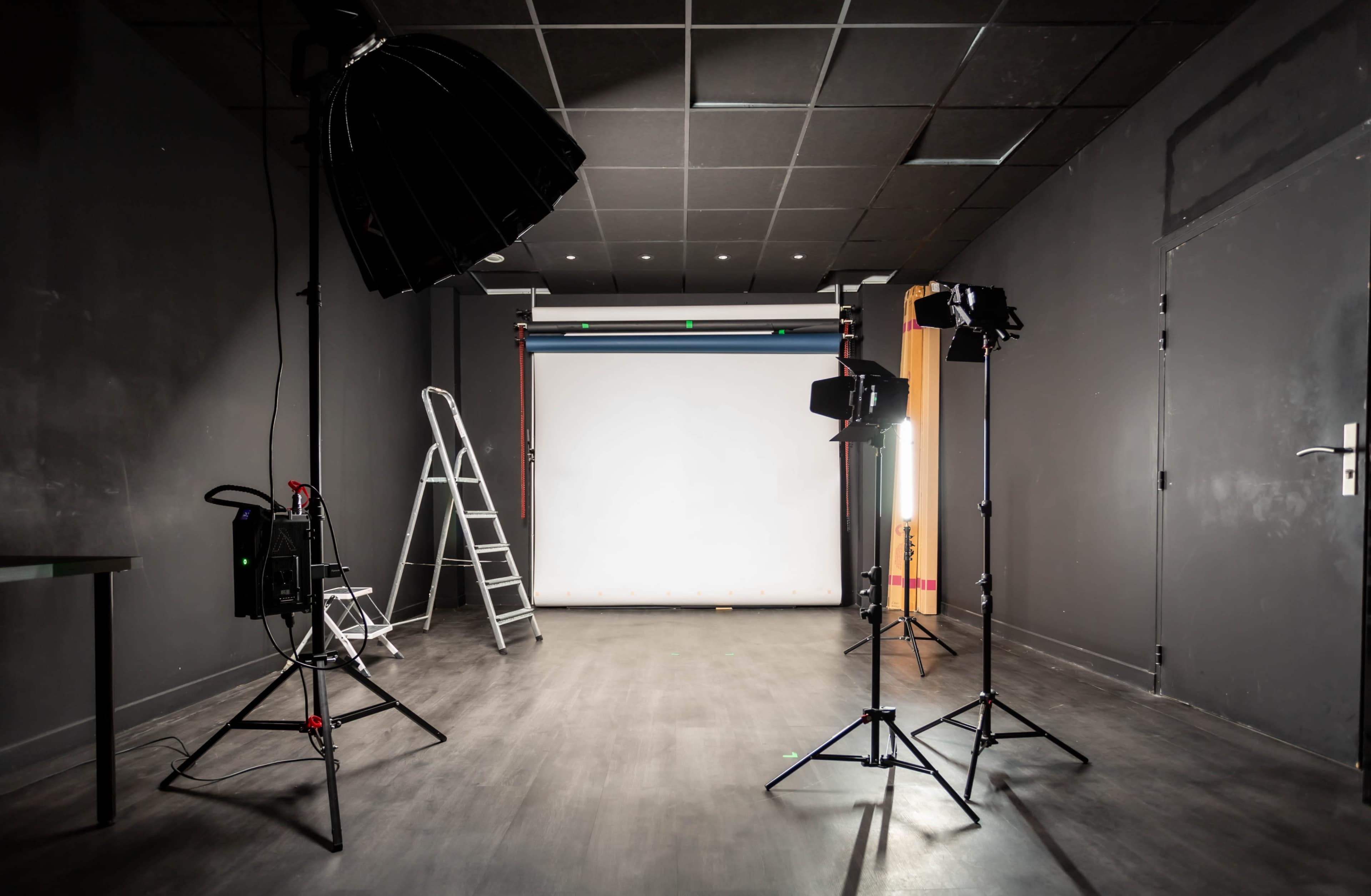 A photography studio setup with lighting equipment, a ladder, and a backdrop.