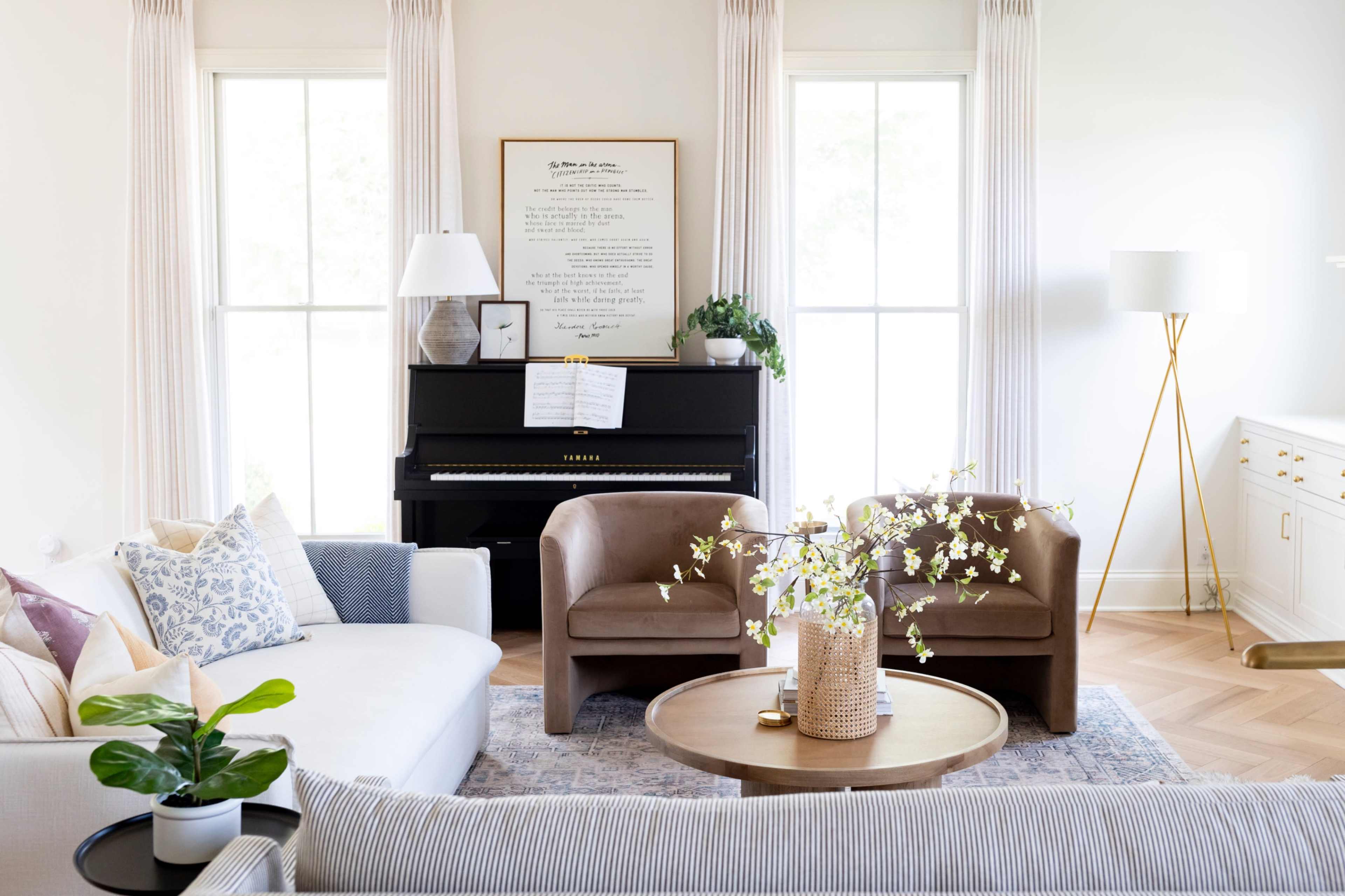 A light and airy living room features a piano, modern furniture, and decorative plants arranged around a coffee table.