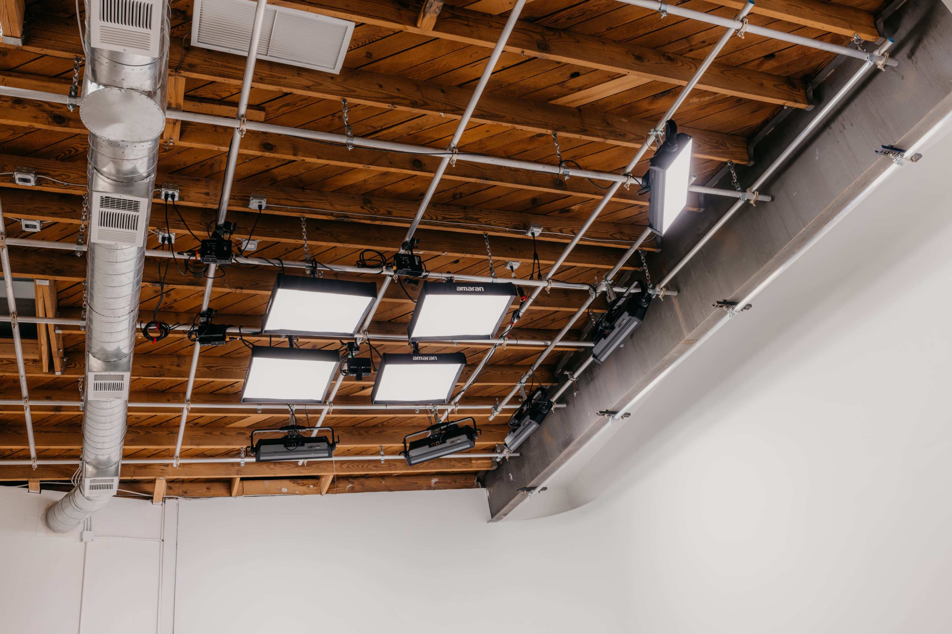 The image shows a studio ceiling with exposed wooden beams and multiple lights arranged on a grid.