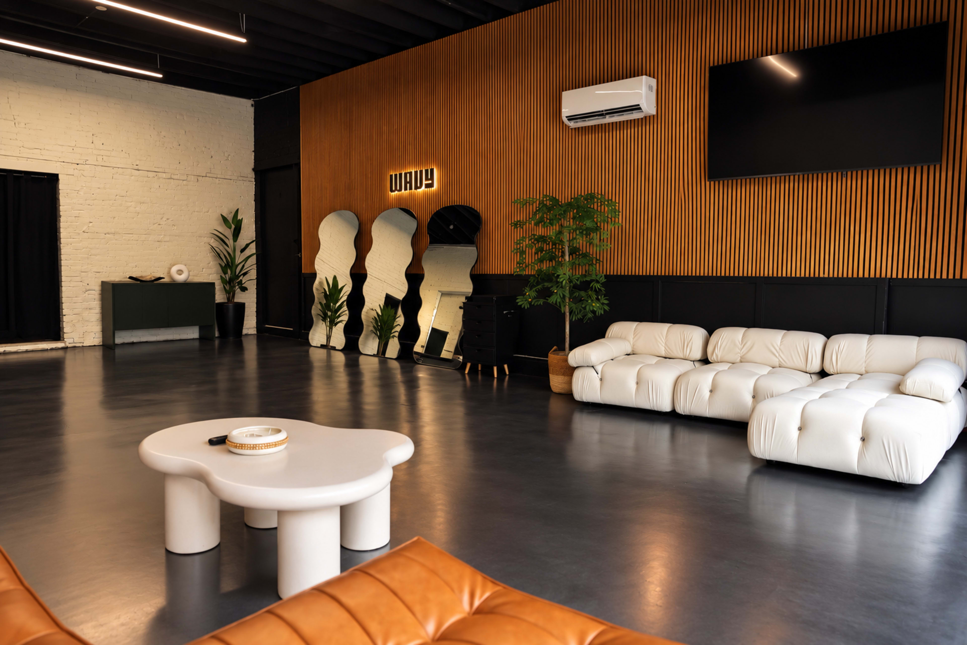 The image shows a modern, minimalist interior featuring a white leather sofa, a round coffee table, and a wooden accent wall with mirrors and plants.