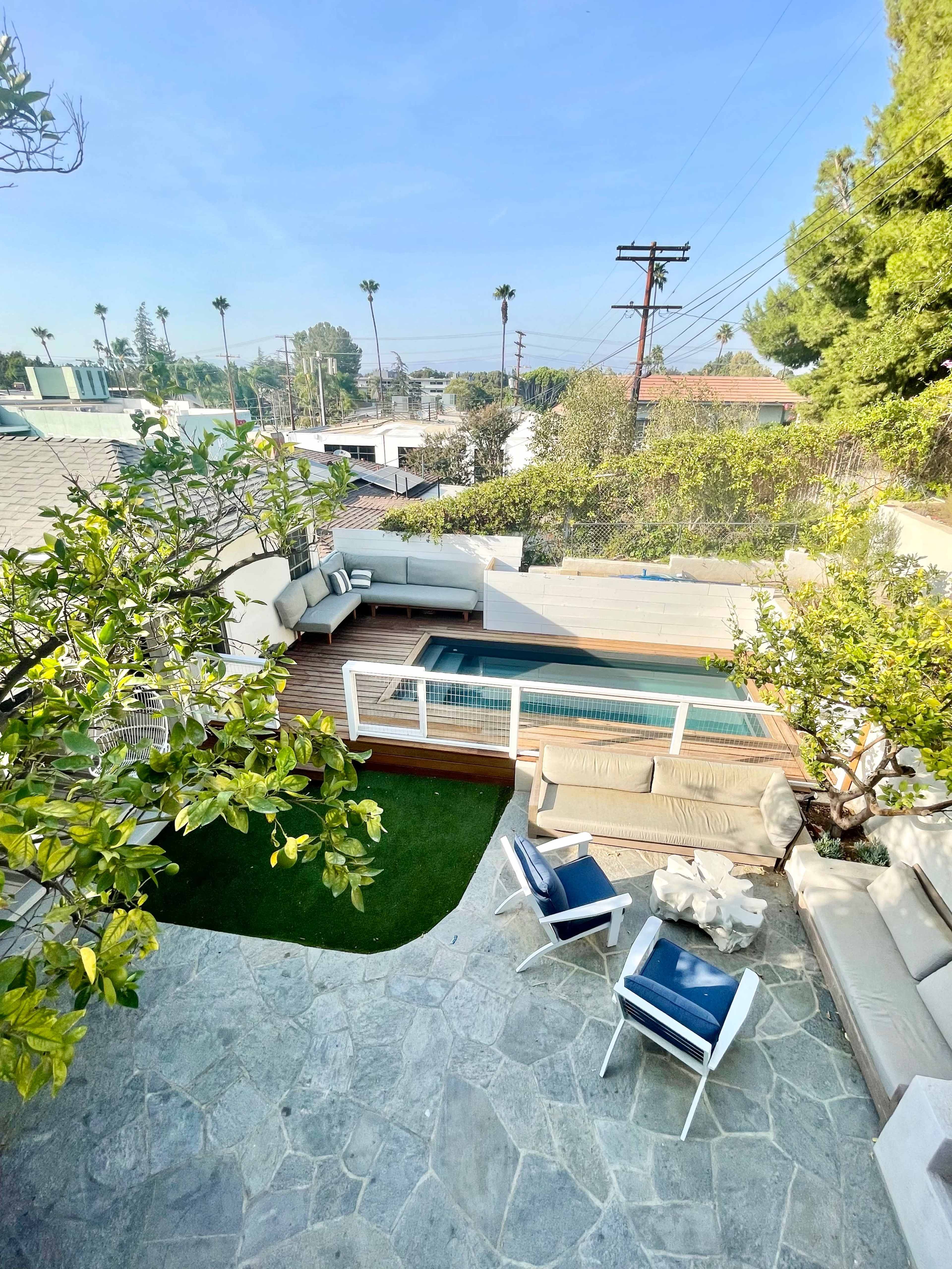 A view of a modern outdoor space featuring a swimming pool, lounge seating, and a landscaped area with trees and greenery.