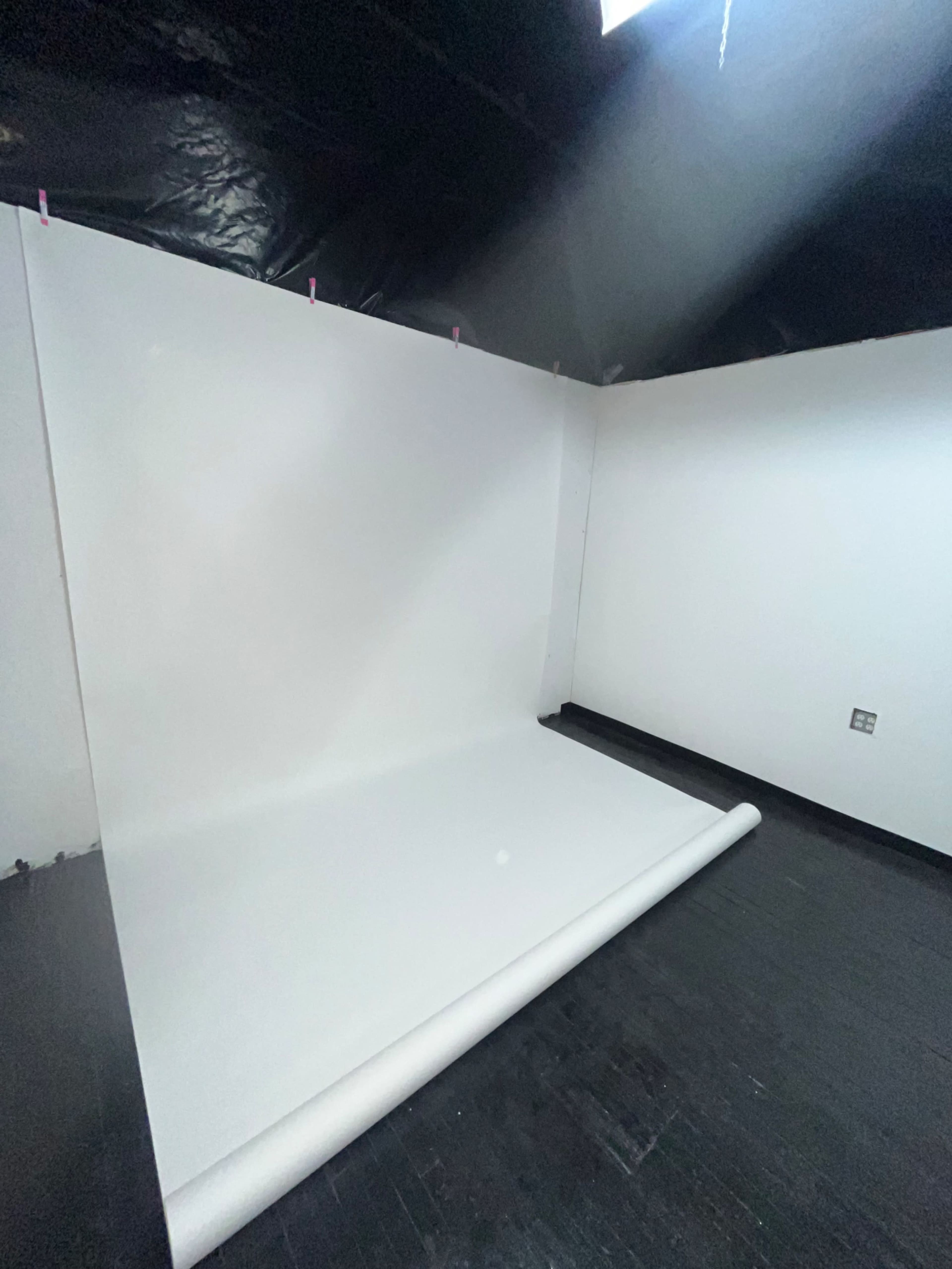 A white backdrop is set up in a dimly lit room with black walls and a wooden floor.