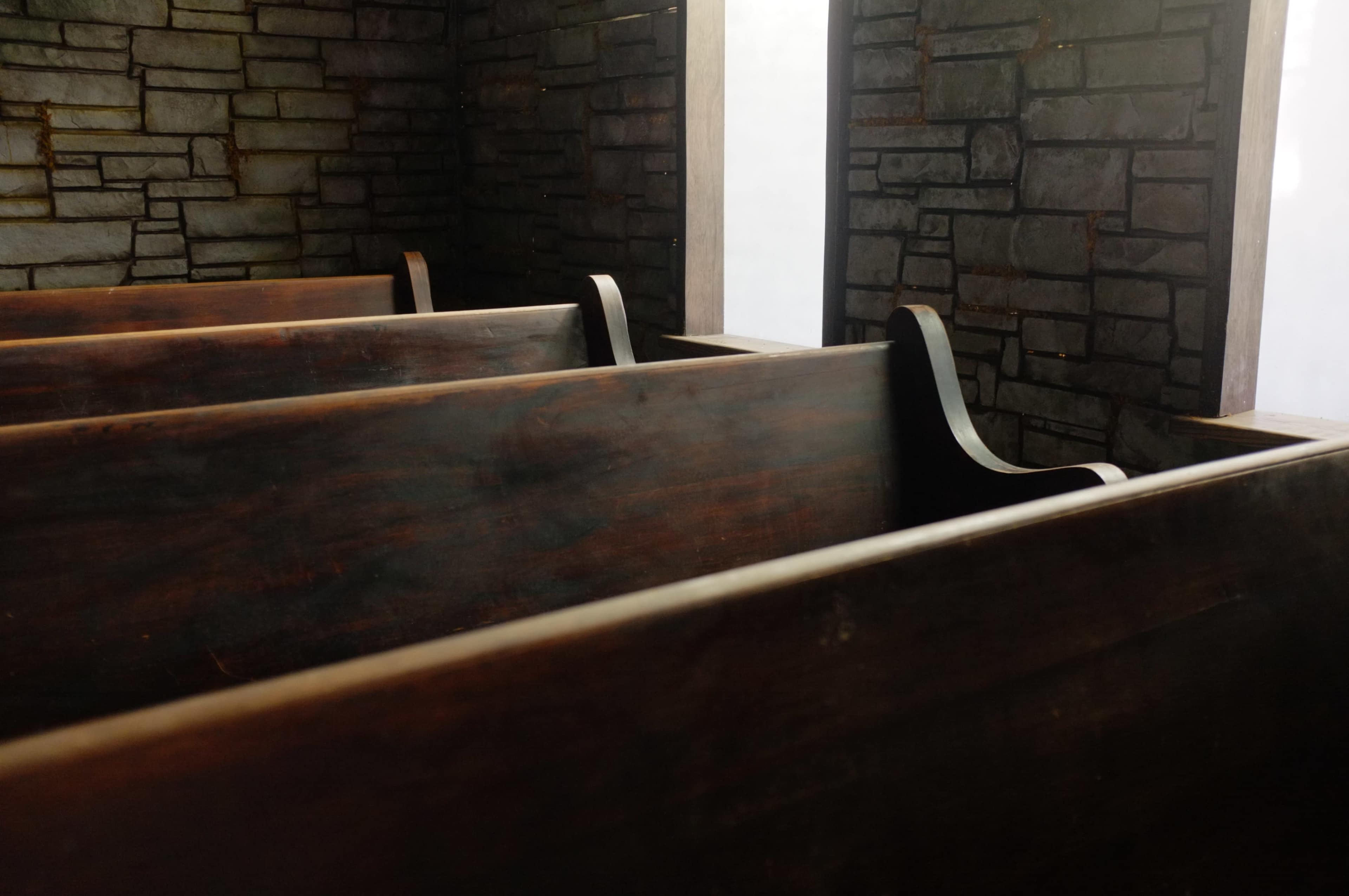 The image shows a dimly lit room with wooden pews arranged along a stone wall.
