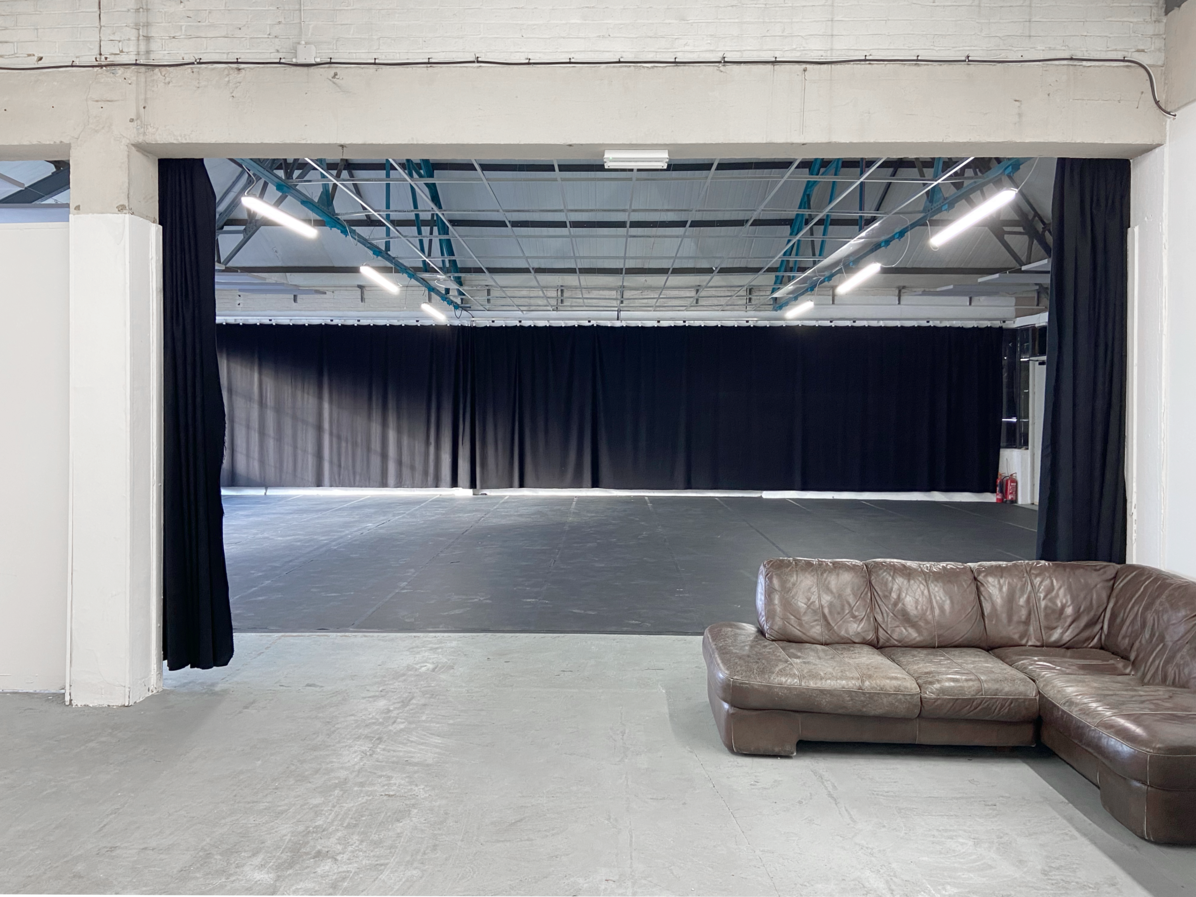 An open space with black curtains on one side and a brown leather couch positioned in front of a polished concrete floor.
