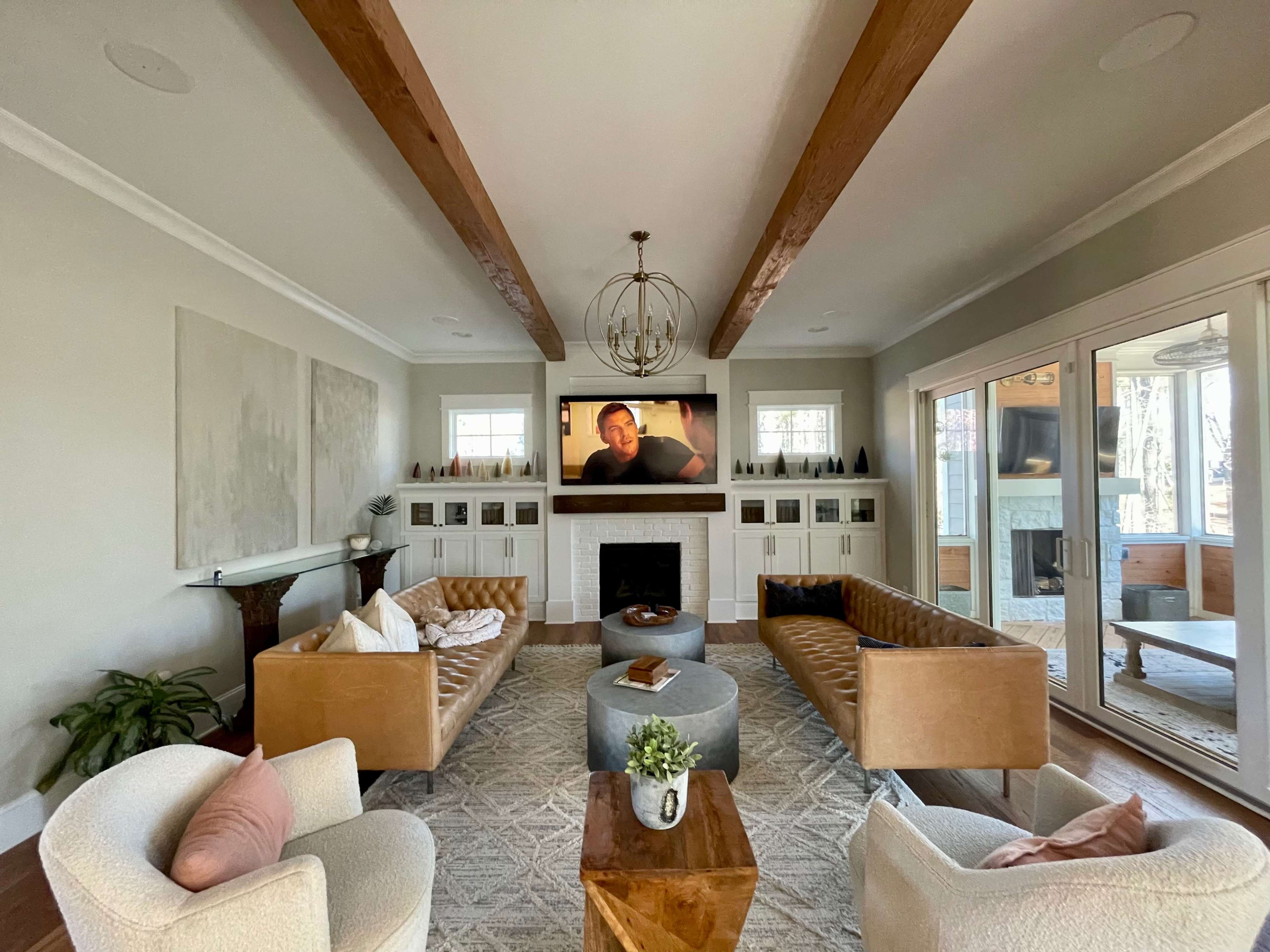 A modern living room features two tan couches facing a round coffee table, with a flat-screen TV mounted above a fireplace surrounded by built-in shelves.