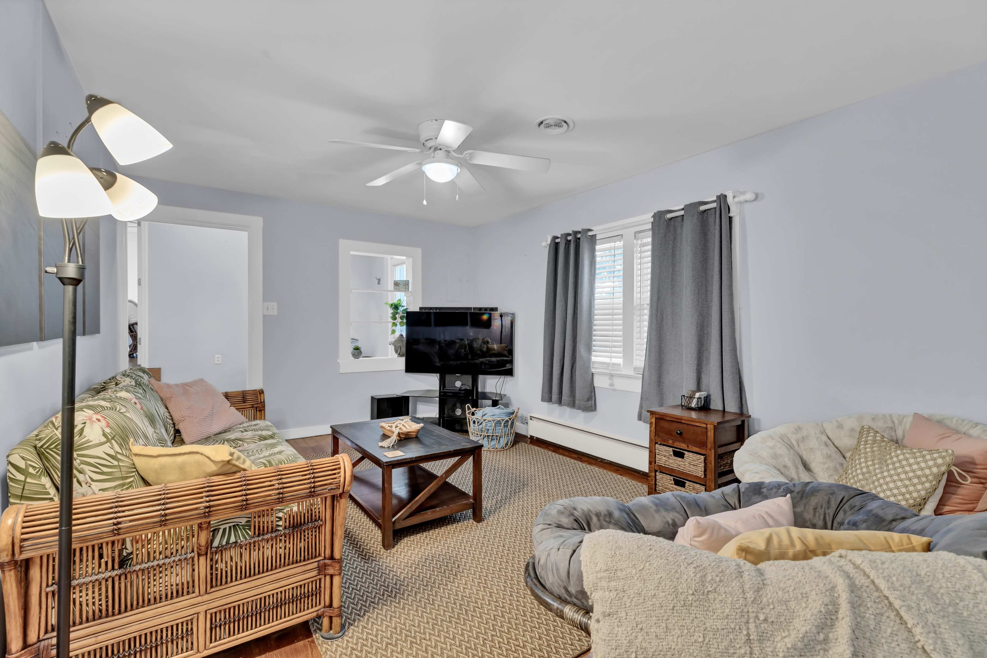The image shows a cozy living room with a television, a coffee table, a patterned sofa, and a large cushioned chair.