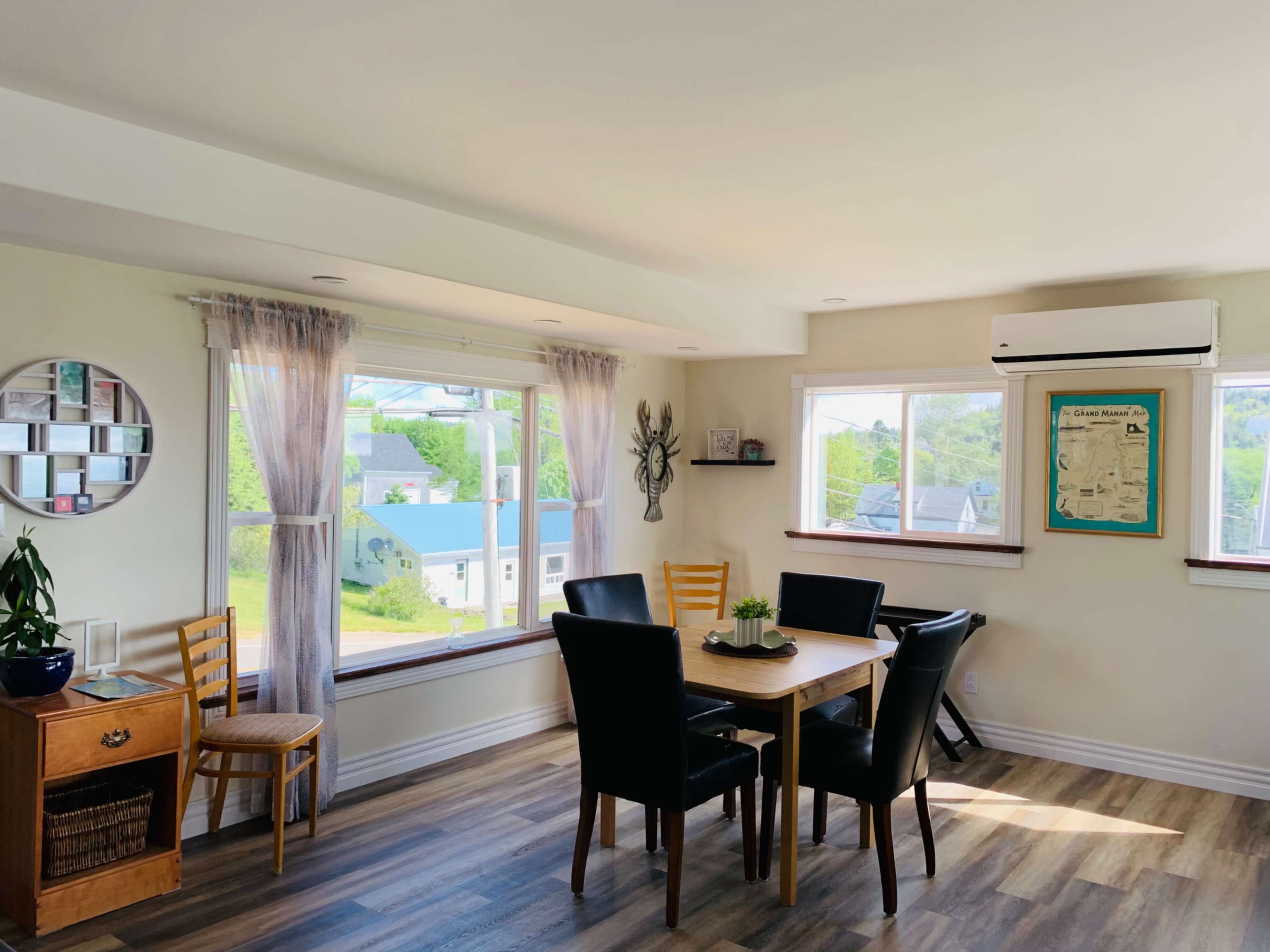 A modern dining area features a wooden table surrounded by black chairs, large windows offering a view of the outside, and light-colored walls.