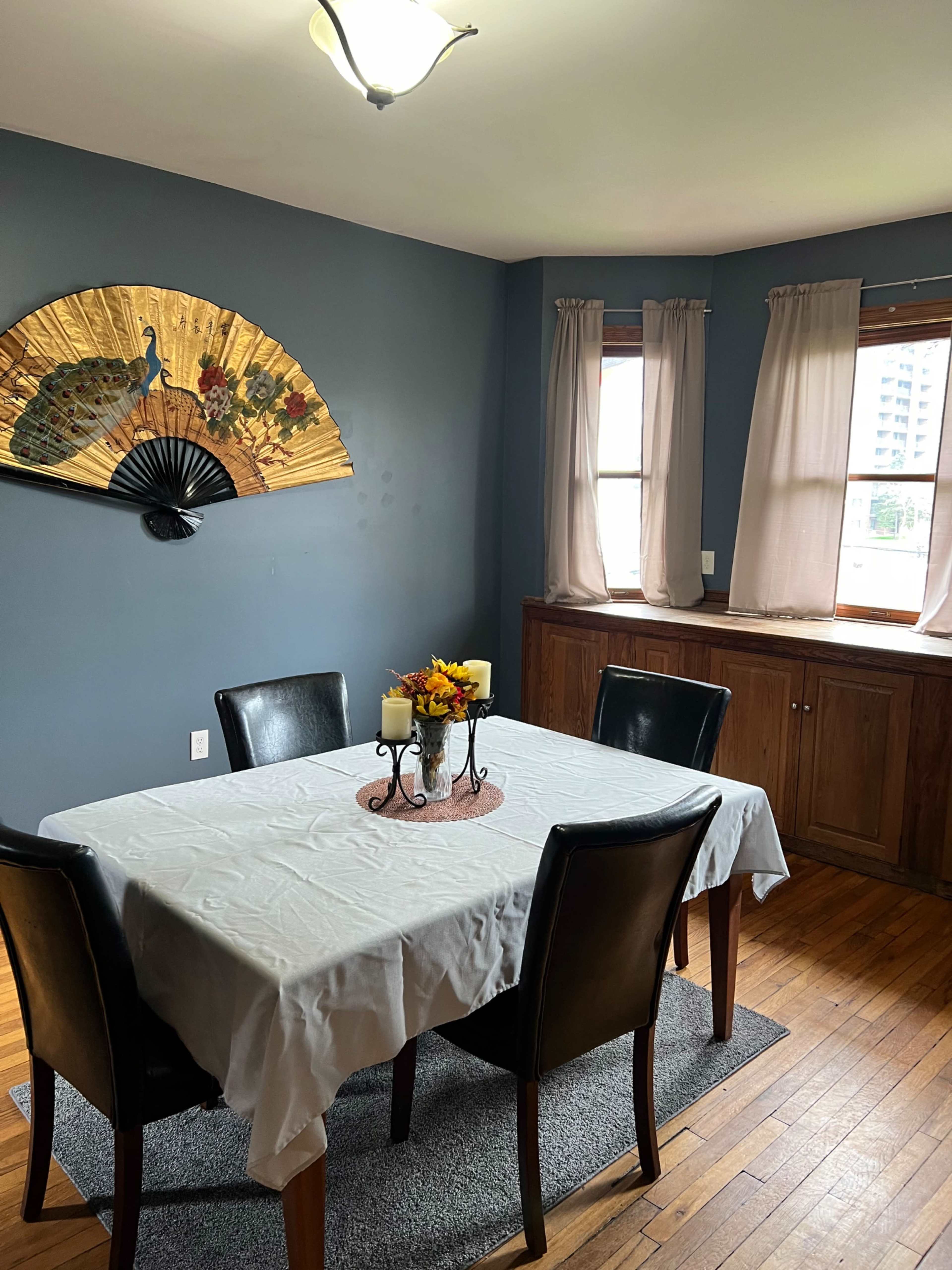 A dining room with a table set for four, surrounded by black chairs, and a decorative fan and curtains on the walls.