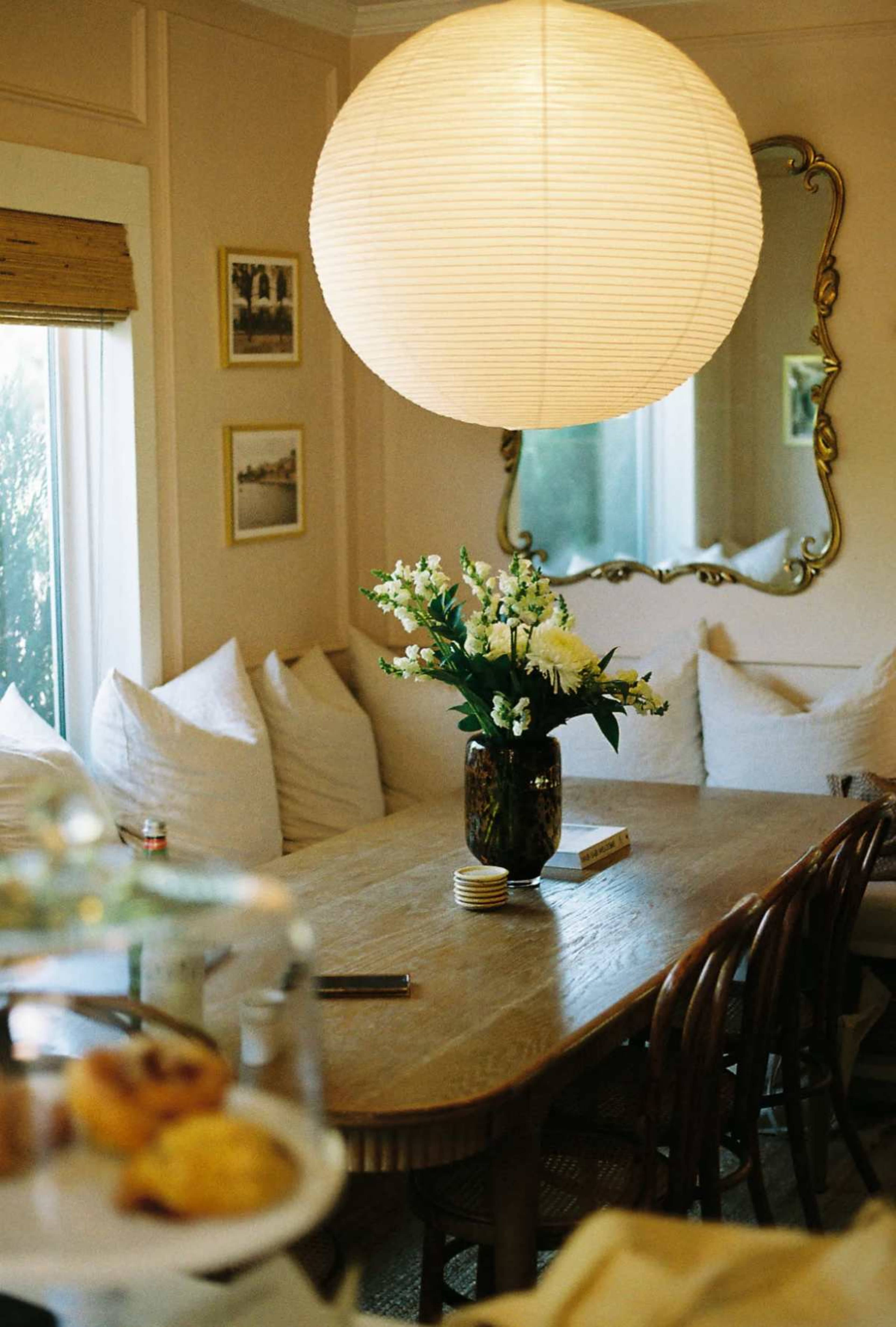 A spacious dining area features a large wooden table surrounded by chairs, with a prominent lantern overhead and a floral arrangement as a centerpiece.