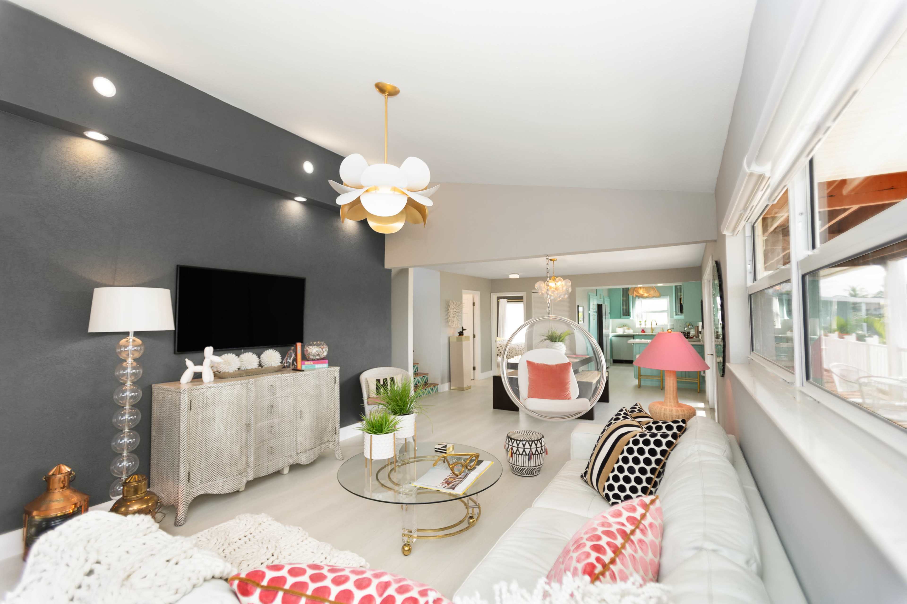 The living room features a light-colored sofa, a glass coffee table, a television on the wall, and a mix of modern lighting fixtures.