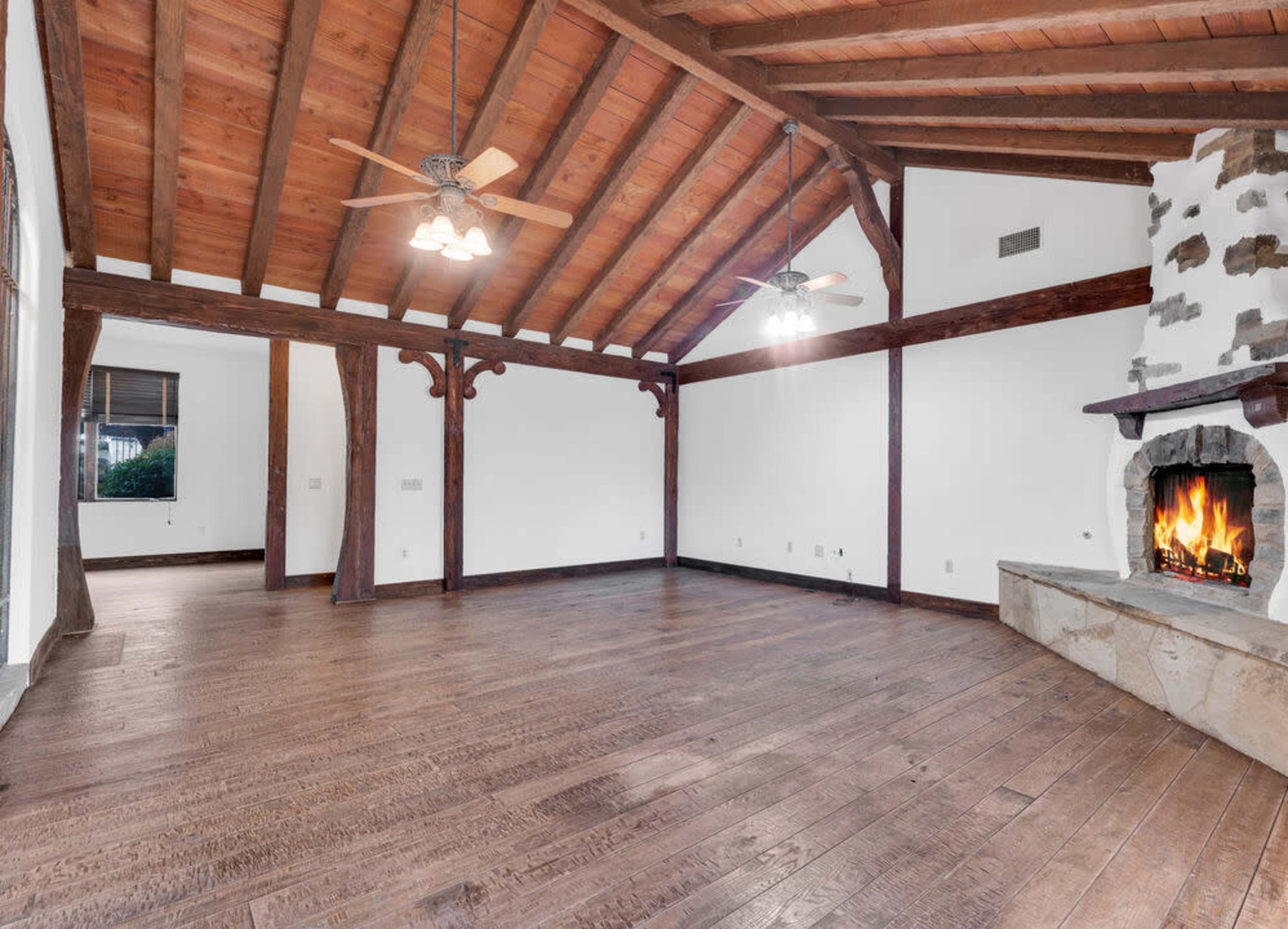 A spacious living room features exposed wooden beams, a stone fireplace, and hardwood floors.