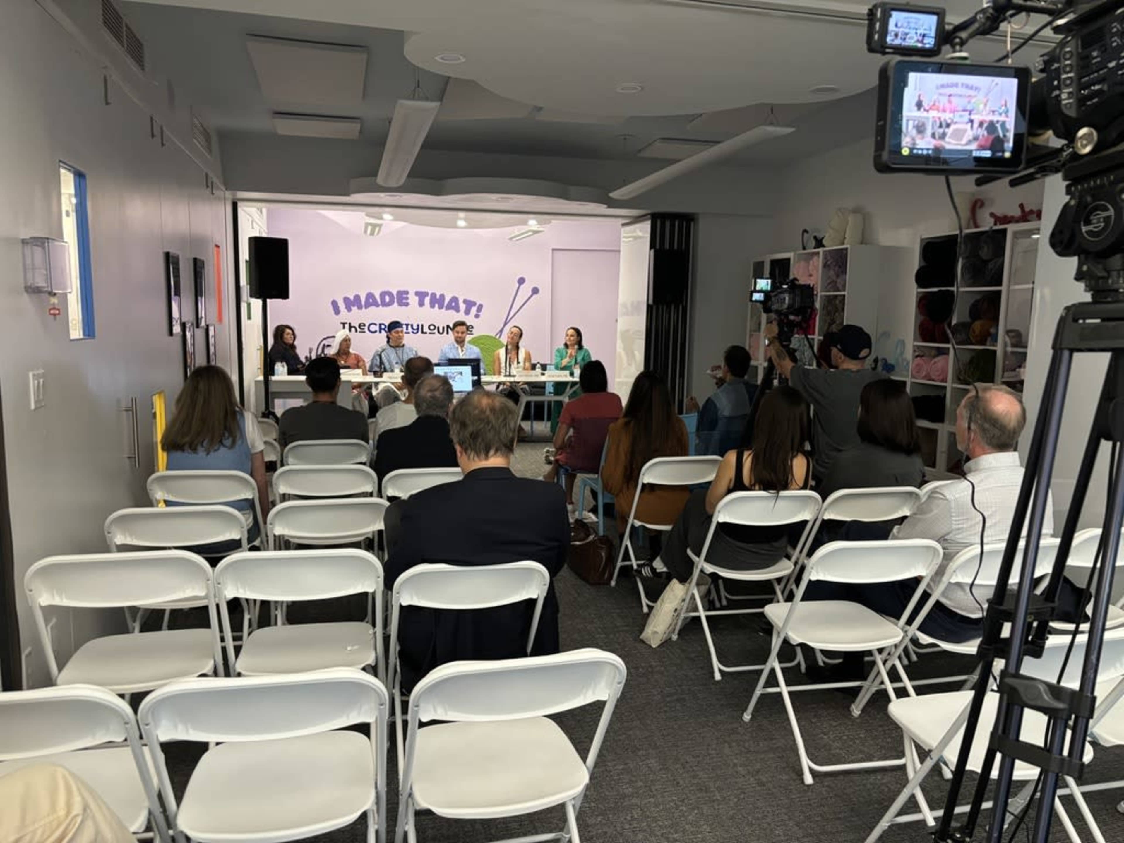 A panel discussion is taking place in a room with a seated audience, featuring four speakers at a table in front of a backdrop that reads "I MADE THAT!"
