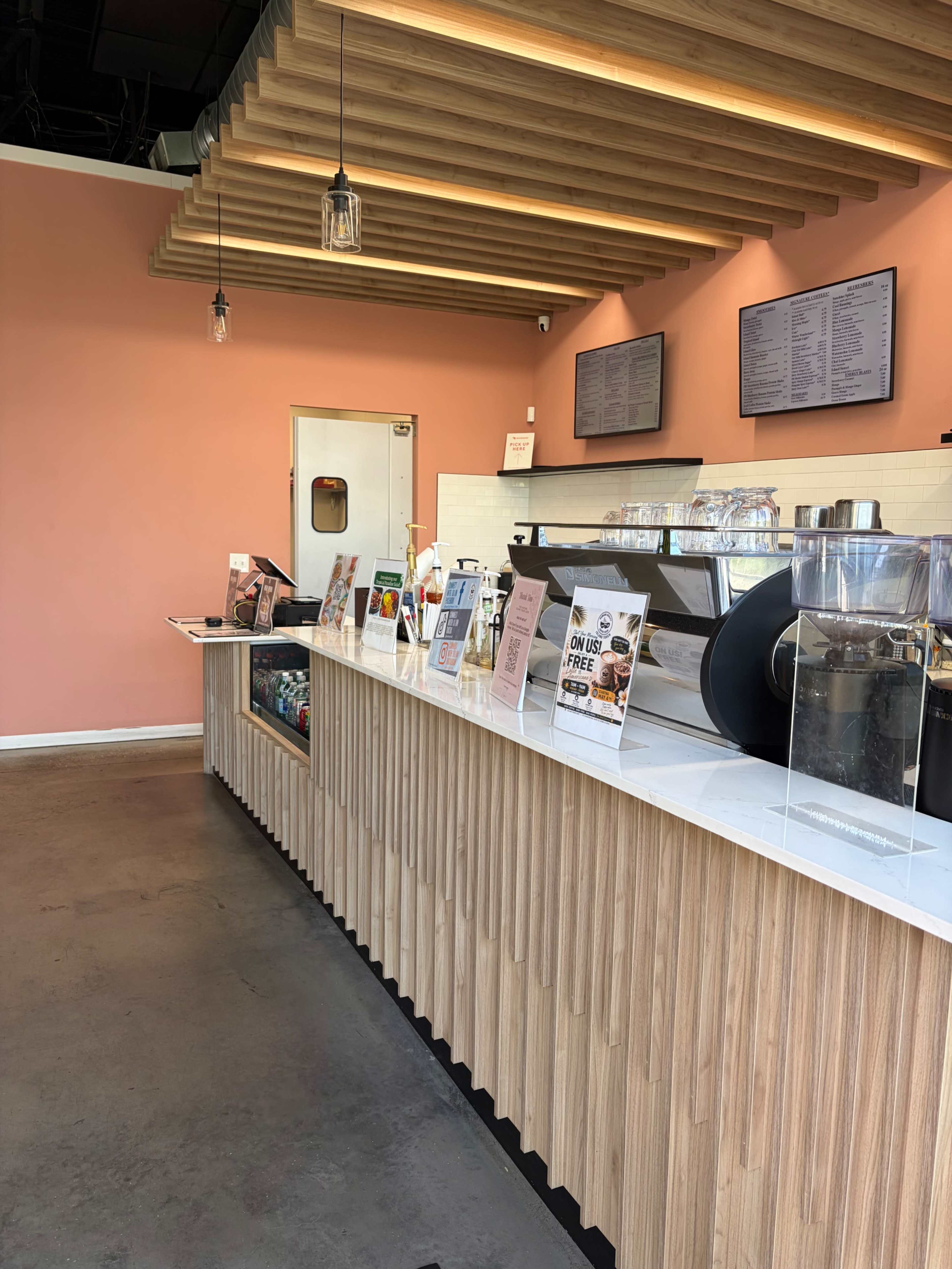 The image shows a coffee shop counter with a wooden finish, various menus displayed, and a coffee machine in the background.