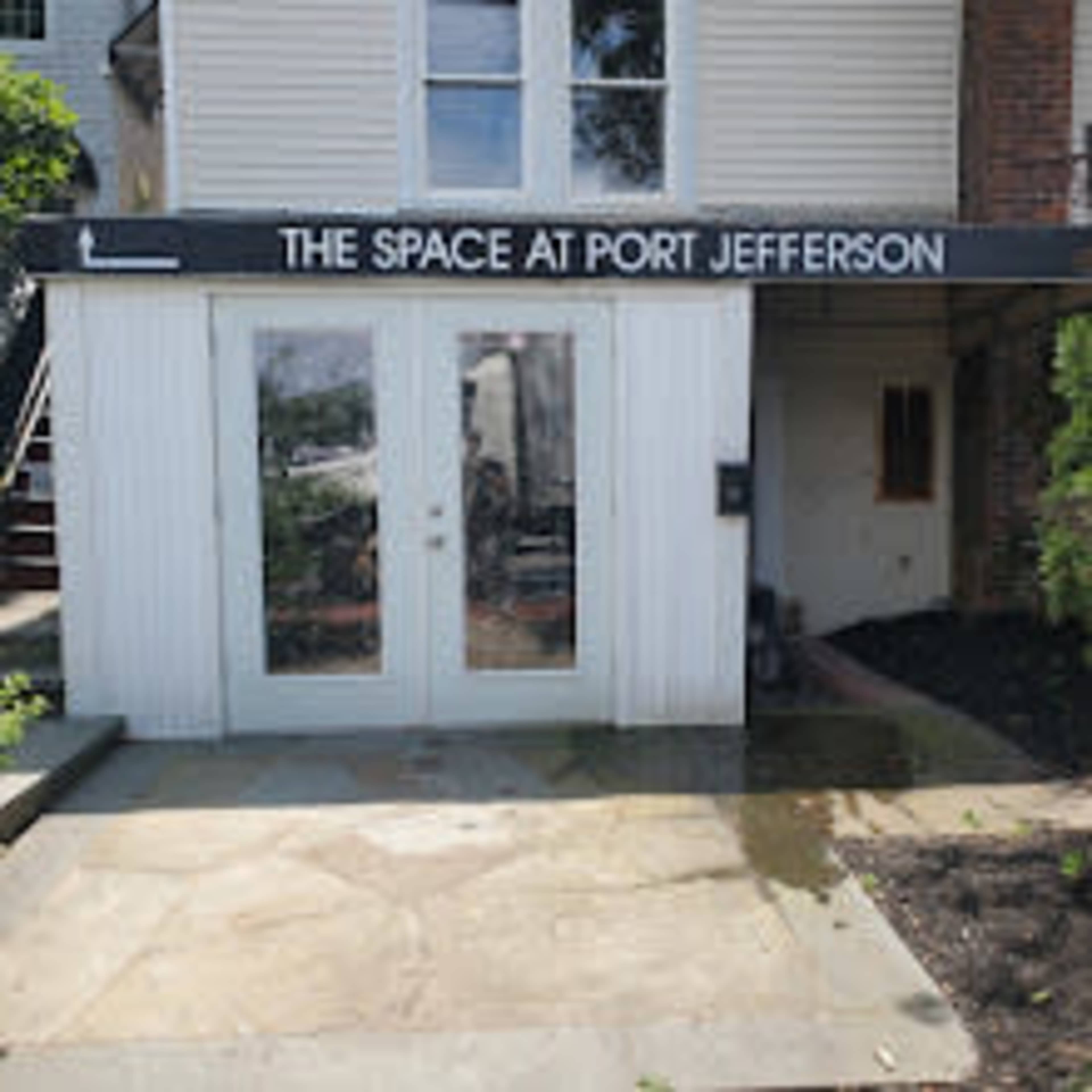 A building entrance with a sign that reads "THE SPACE AT PORT JEFFERSON" above double doors.