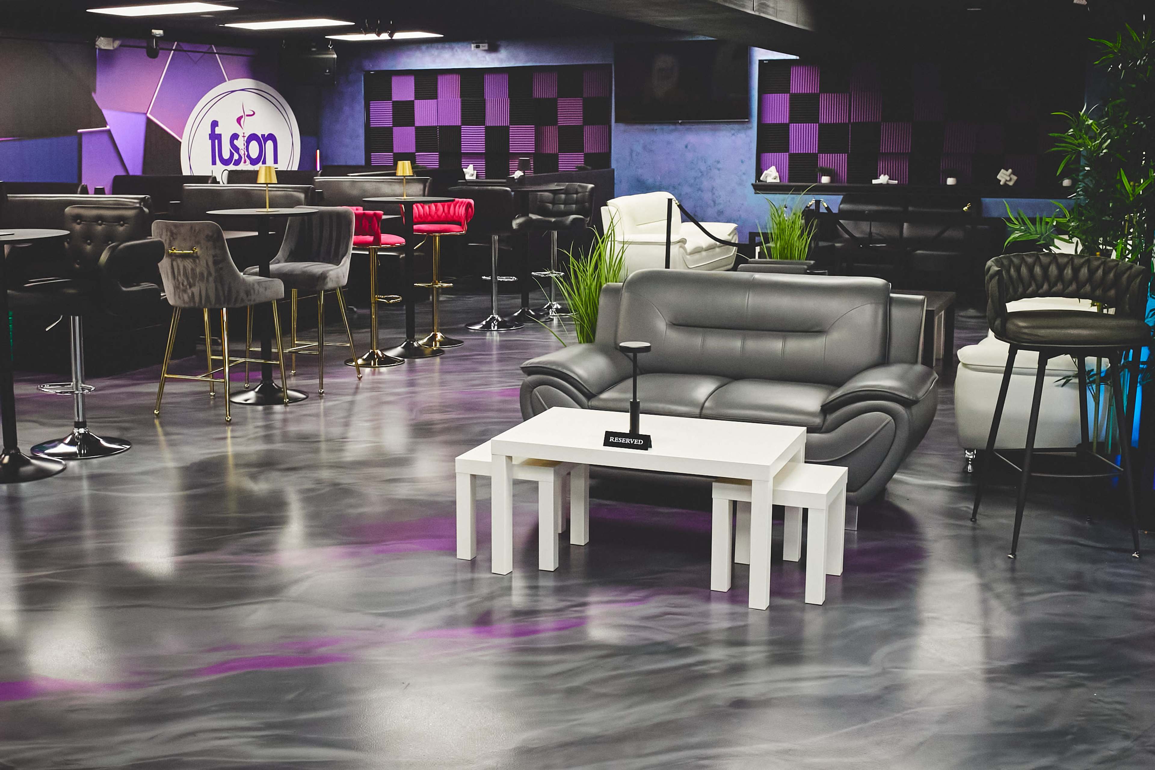 The image shows a modern lounge area featuring a gray sofa, white tables, and various seating arrangements with a bar in the background.