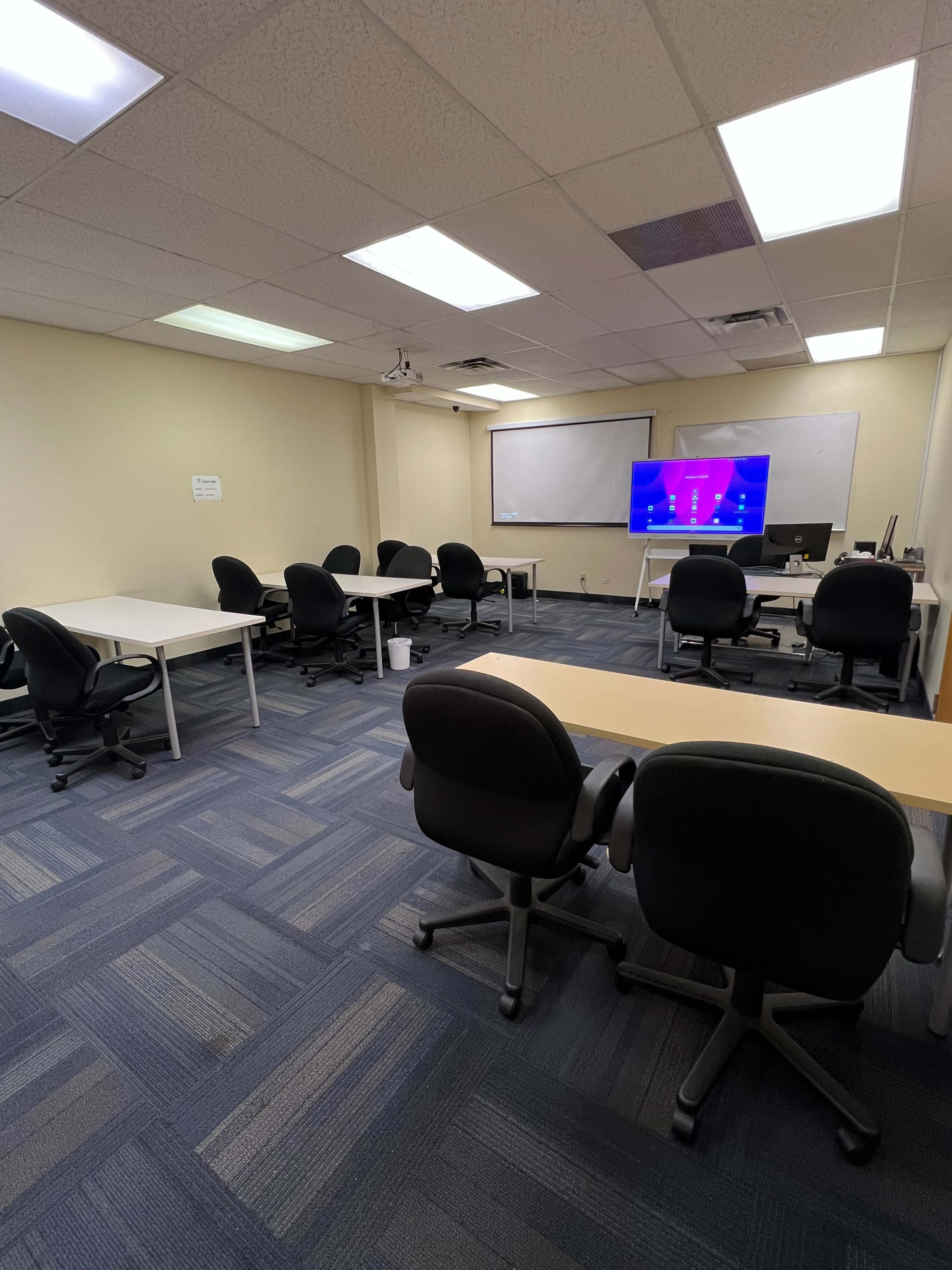 A conference room features several tables and chairs arranged around a presentation screen.