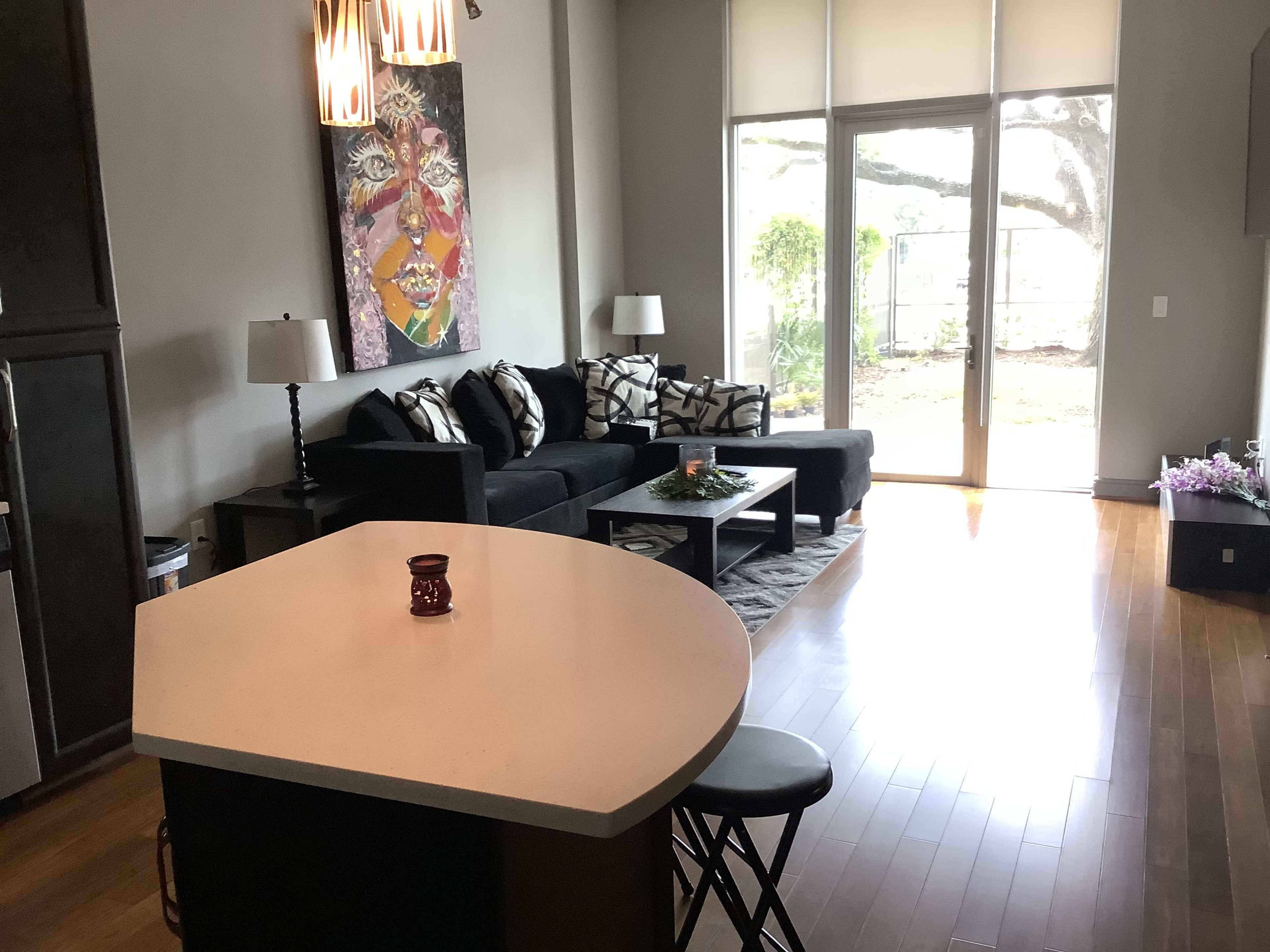 A modern living room with a black sofa, a coffee table, and a view of a garden through large windows.