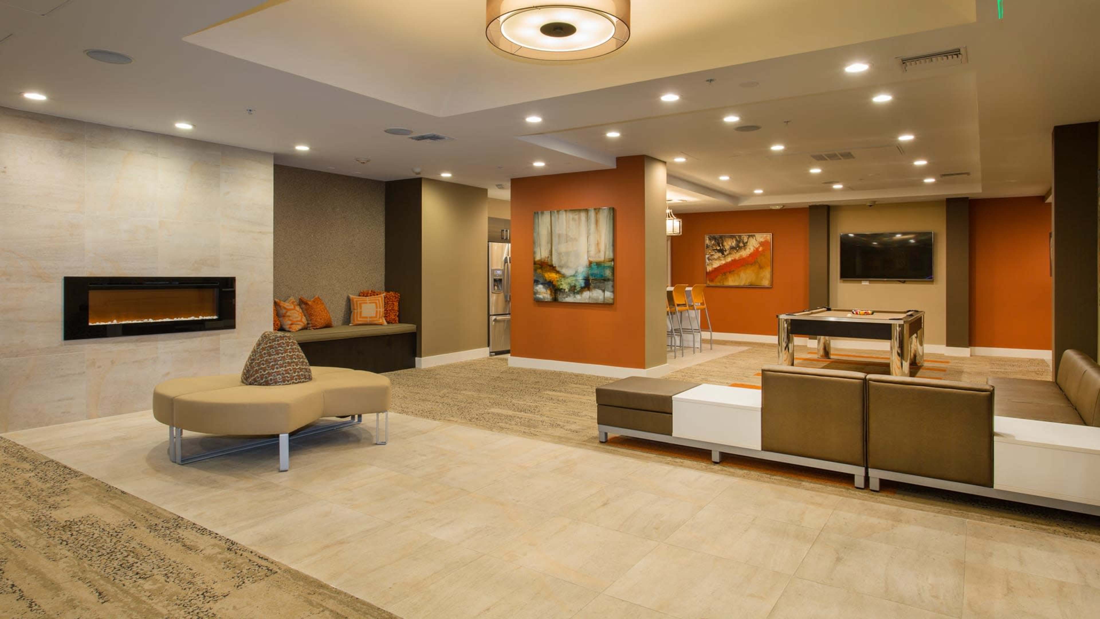 The image shows a modern lounge area with a seating arrangement, a wall-mounted television, and a fireplace.