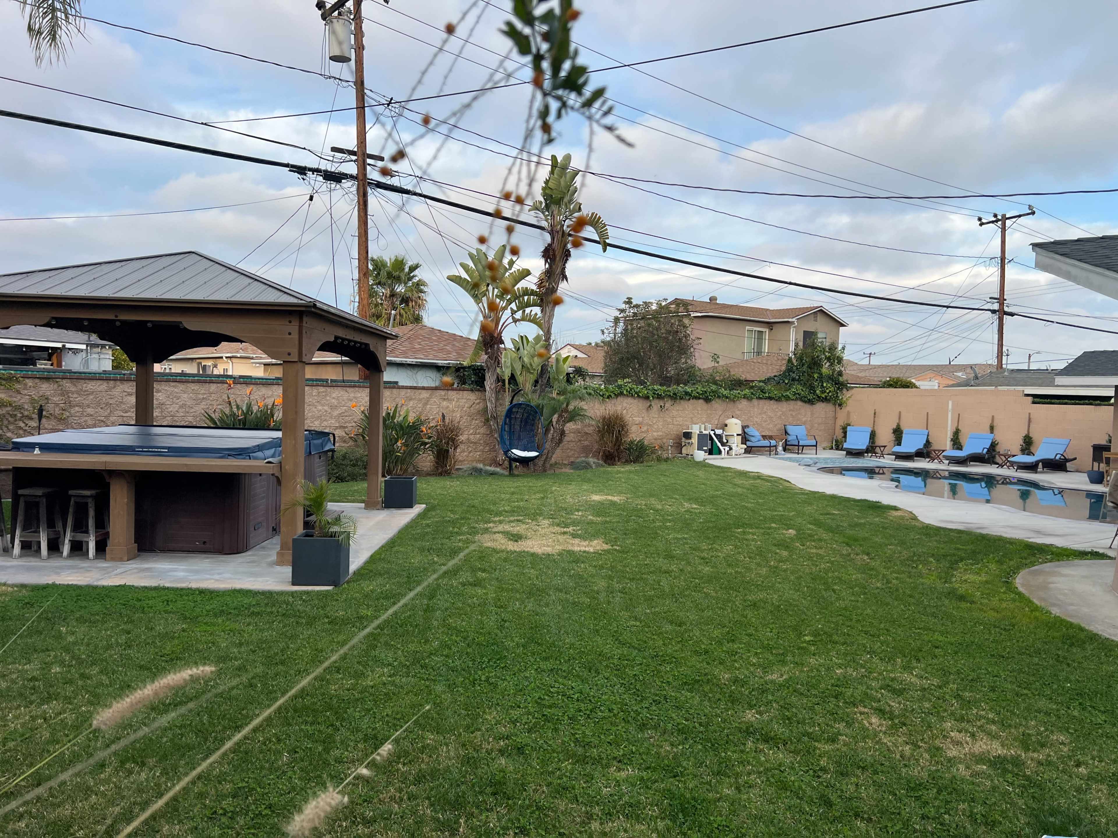 A backyard area with a gazebo, hot tub, and several lounge chairs arranged on a green lawn.