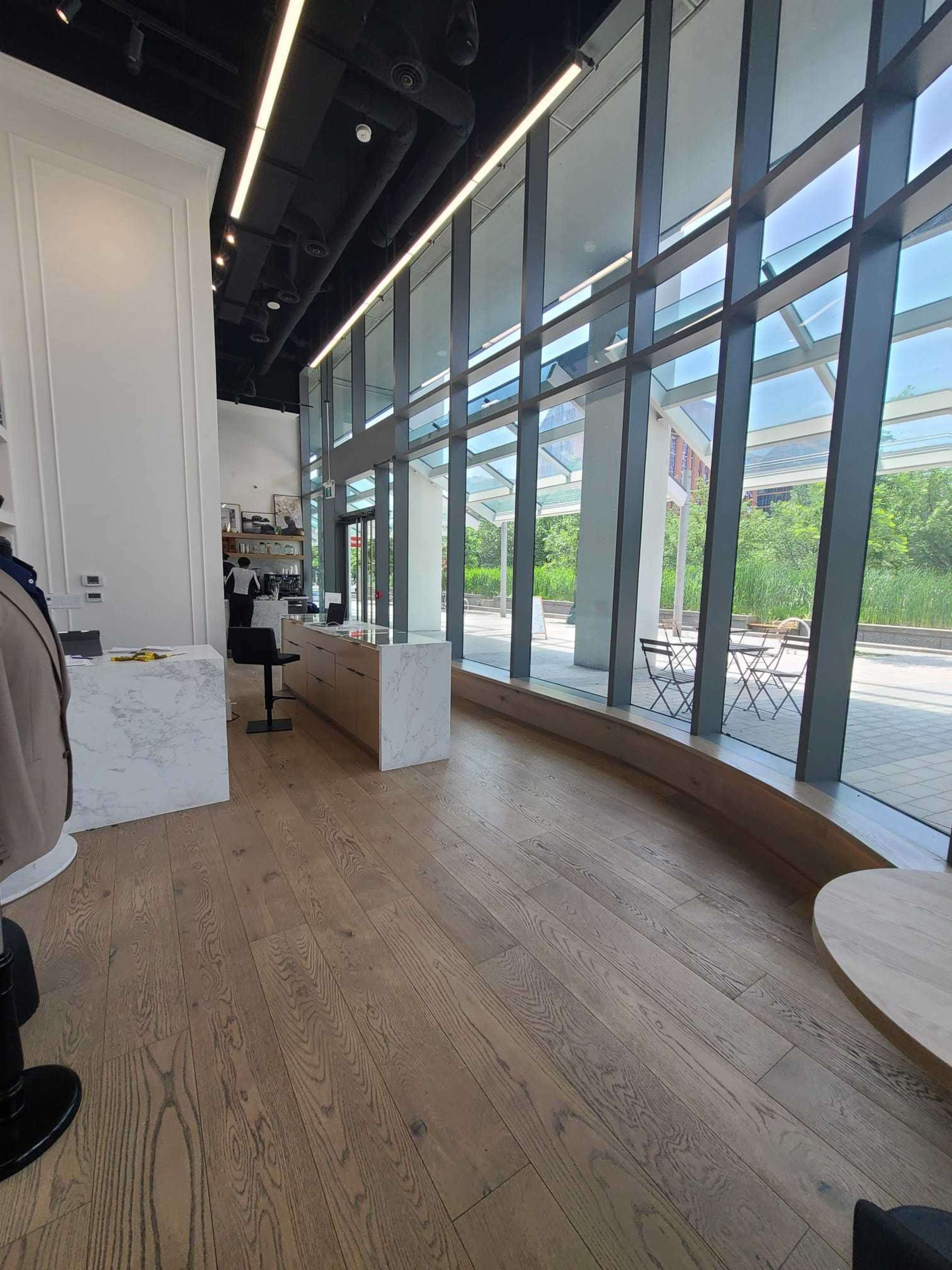 The image shows a modern retail space with large glass windows, minimalistic white furnishings, and wooden flooring.