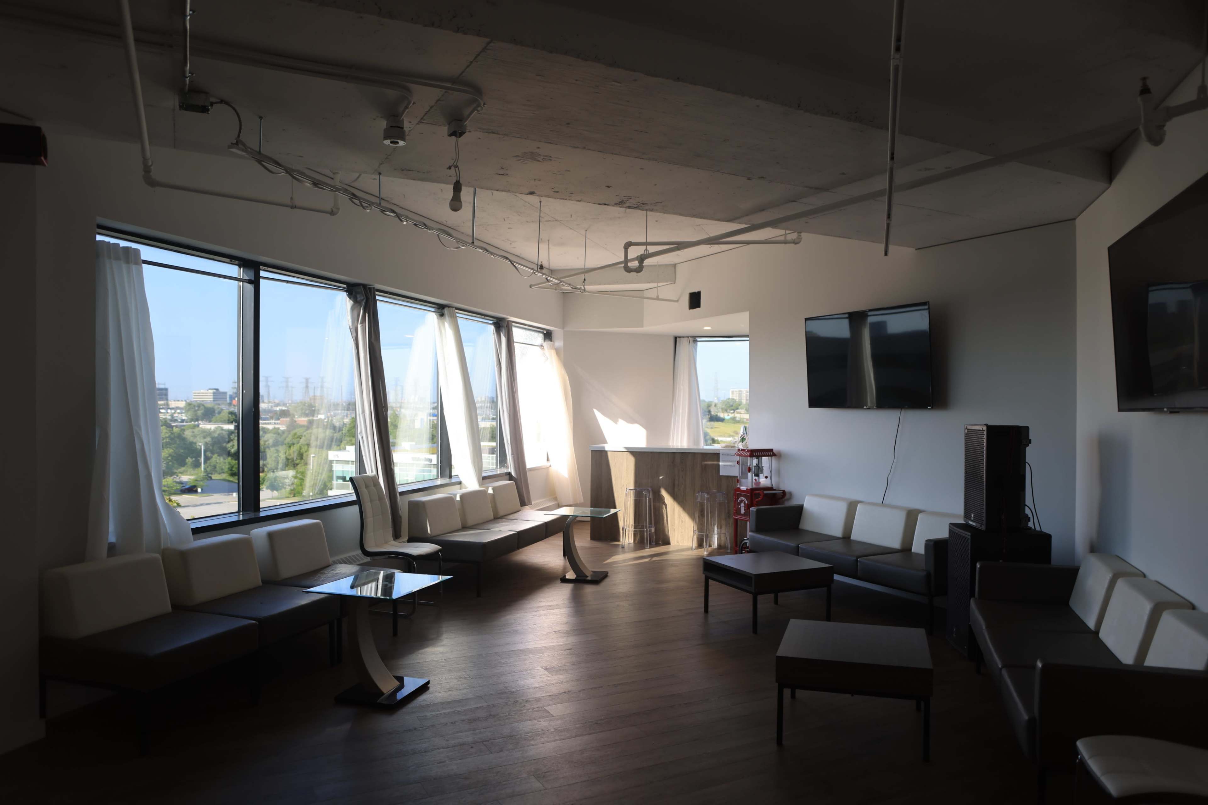 The image shows a modern lounge area with large windows, featuring multiple seating arrangements and a bar counter in a well-lit space.