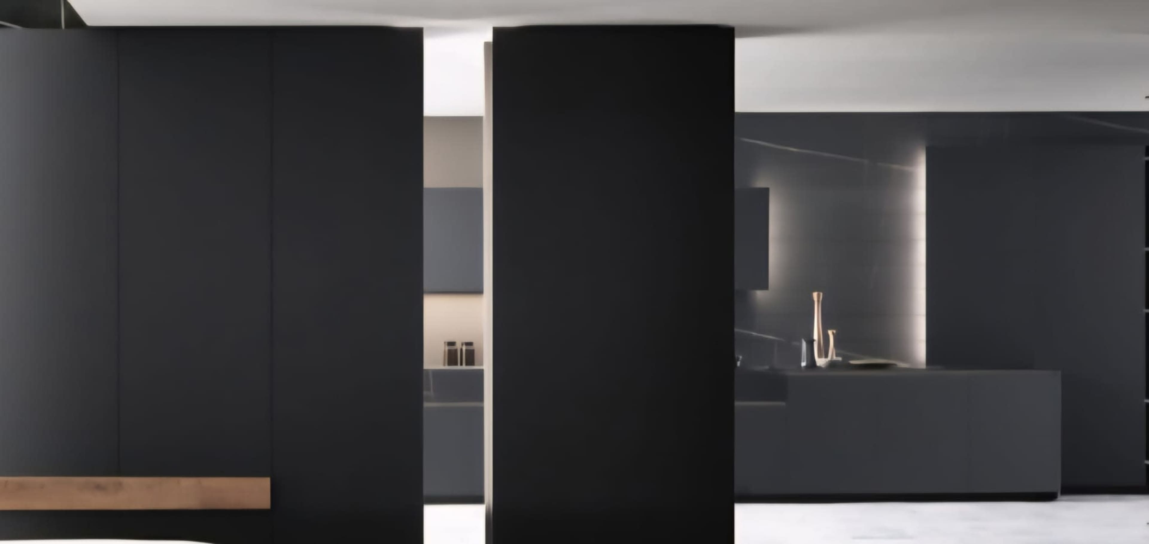 The image shows a modern, minimalistic kitchen with dark cabinetry and two prominent black columns separating the space.
