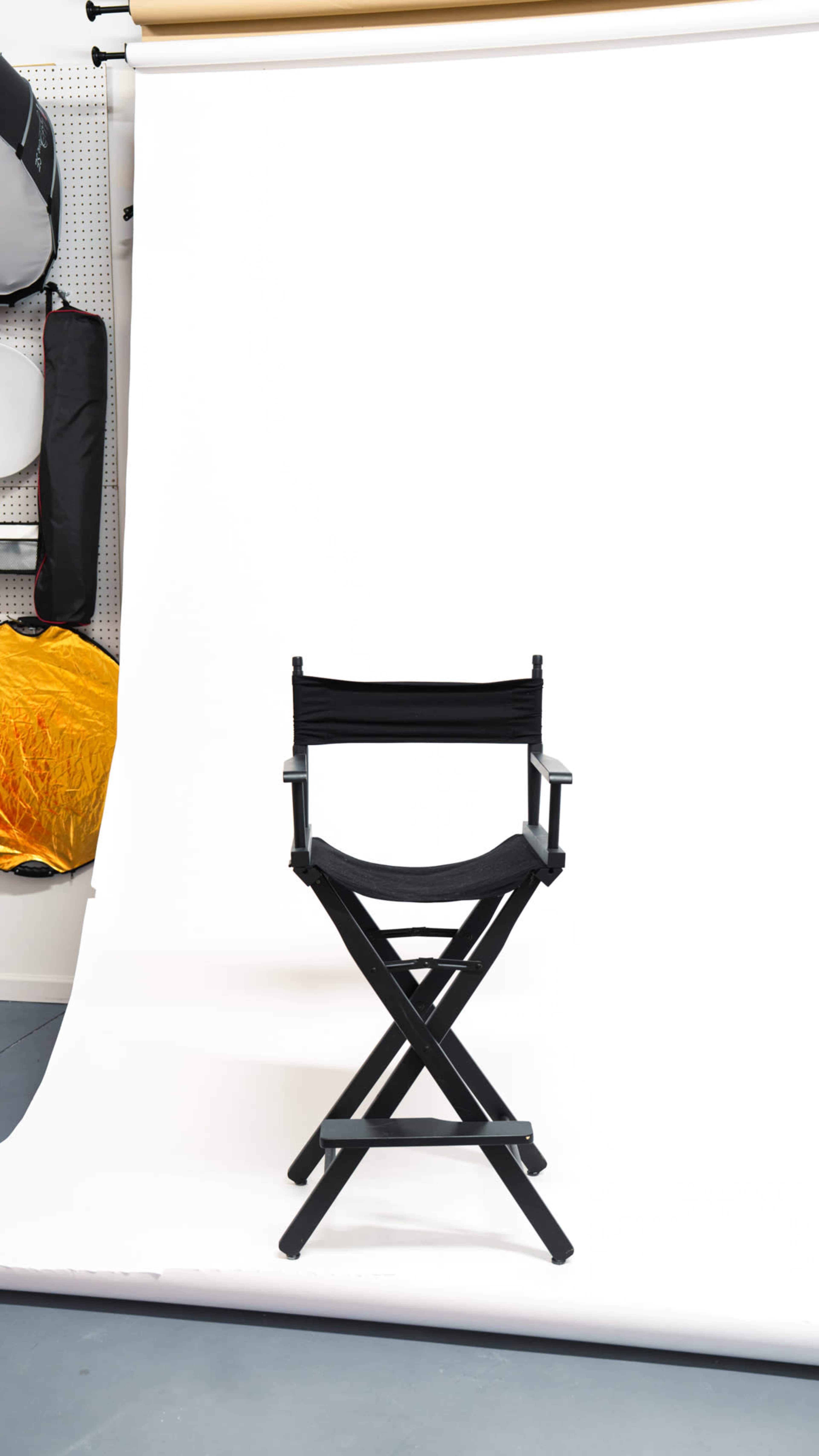 A black director's chair stands prominently in front of a white backdrop.