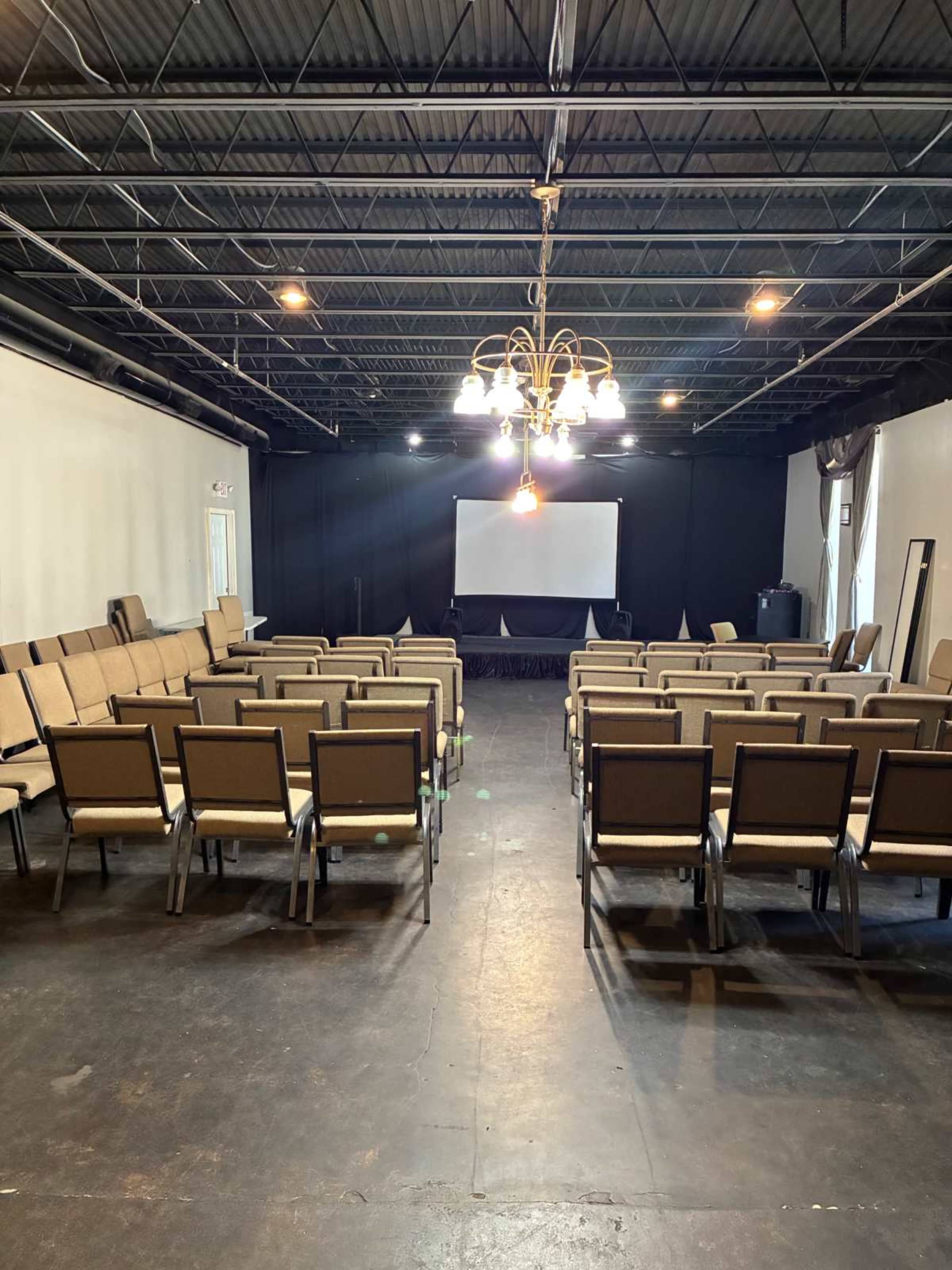 The image shows an empty auditorium with rows of chairs facing a projection screen at the front.