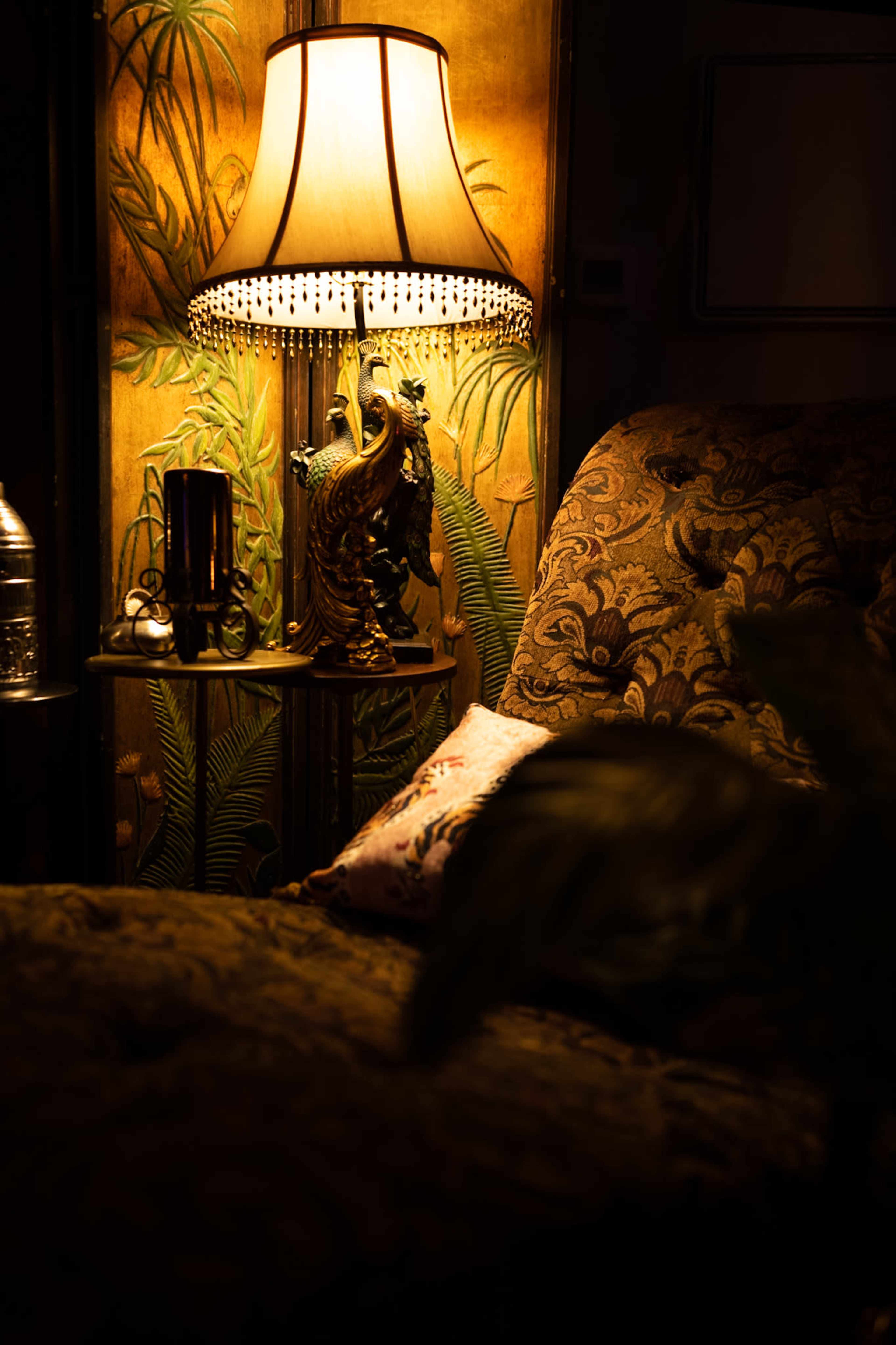 The image depicts a lamp casting warm light on a patterned armchair beside a decorative figurine and a water bottle.