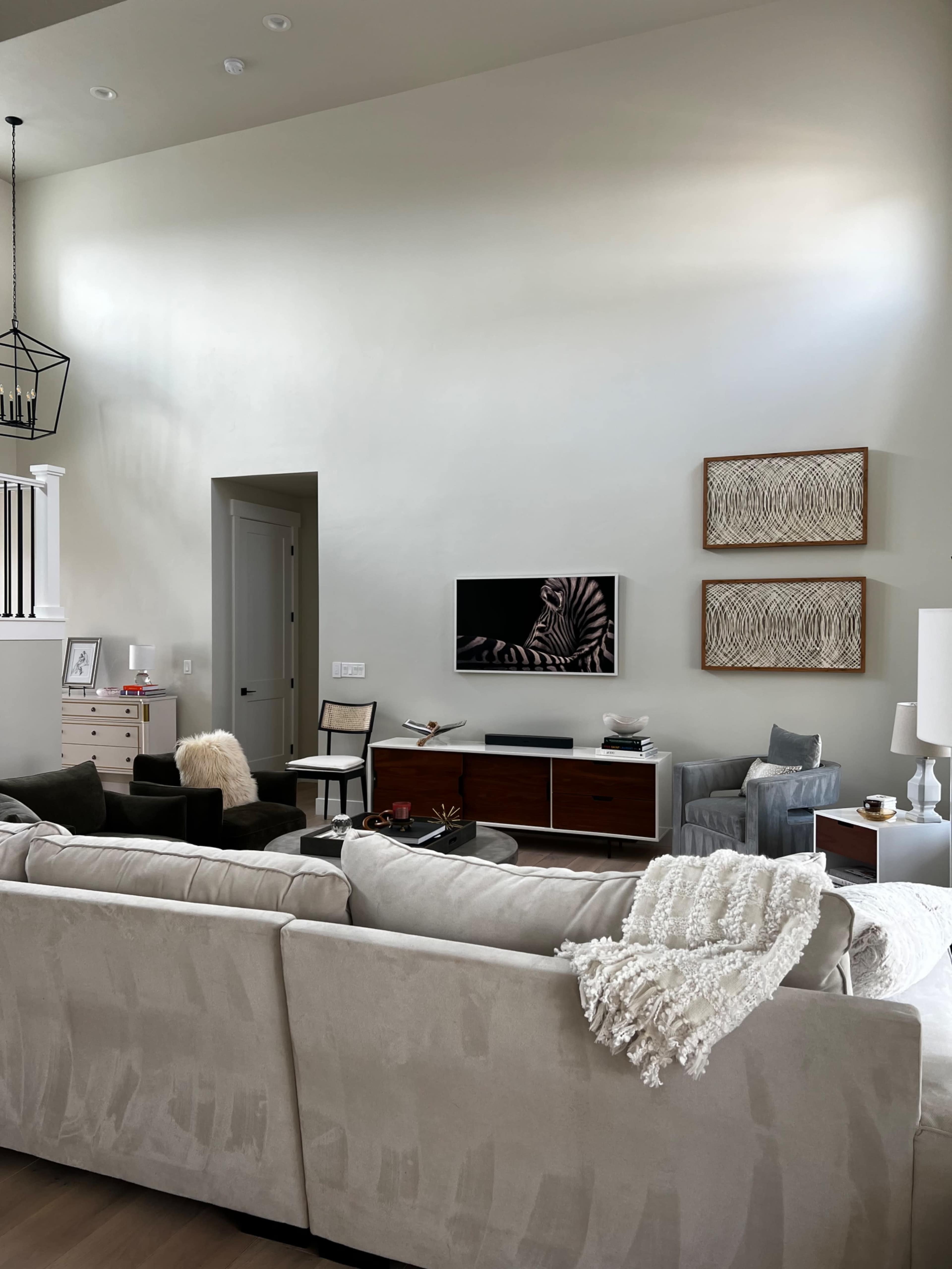 The image shows a modern living room with a large sectional sofa, a coffee table, a television mounted on the wall, and various decorative elements including artwork and furniture.