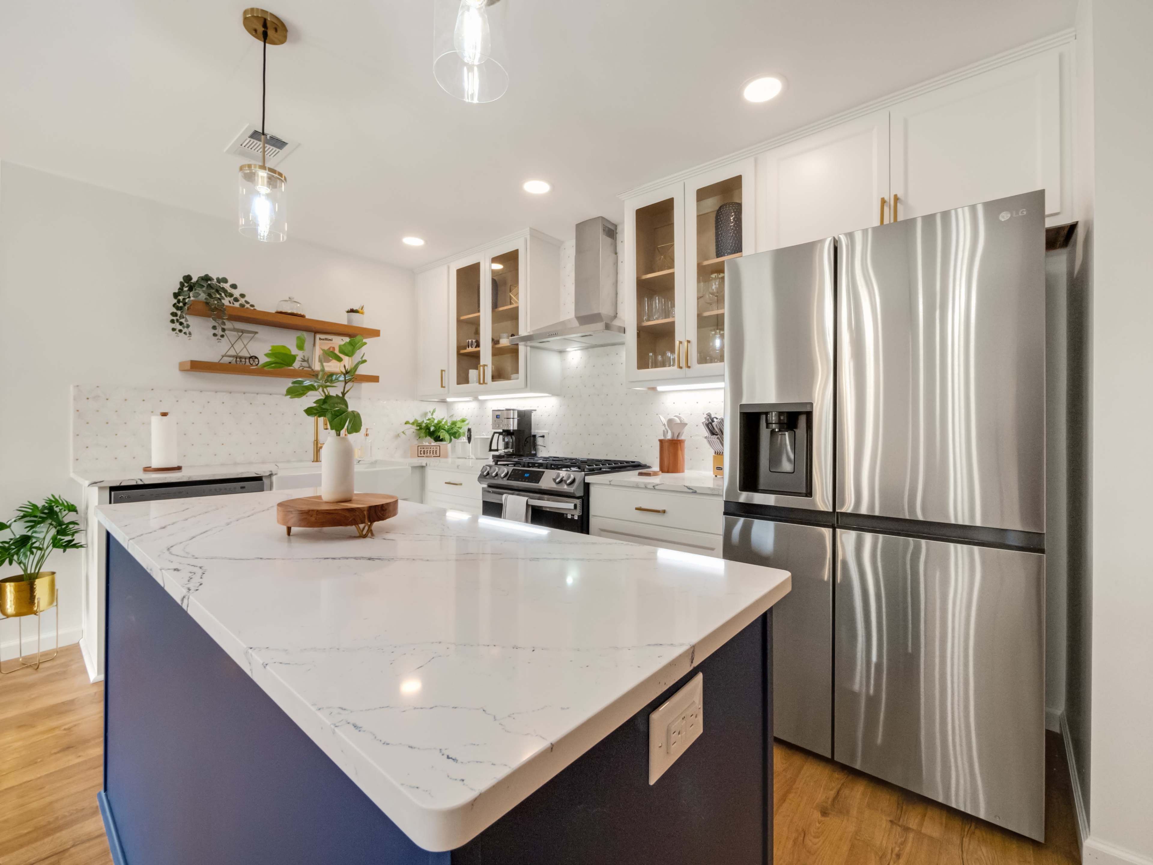 The image shows a modern kitchen featuring a large island with a marble countertop, stainless steel appliances, and white cabinetry.