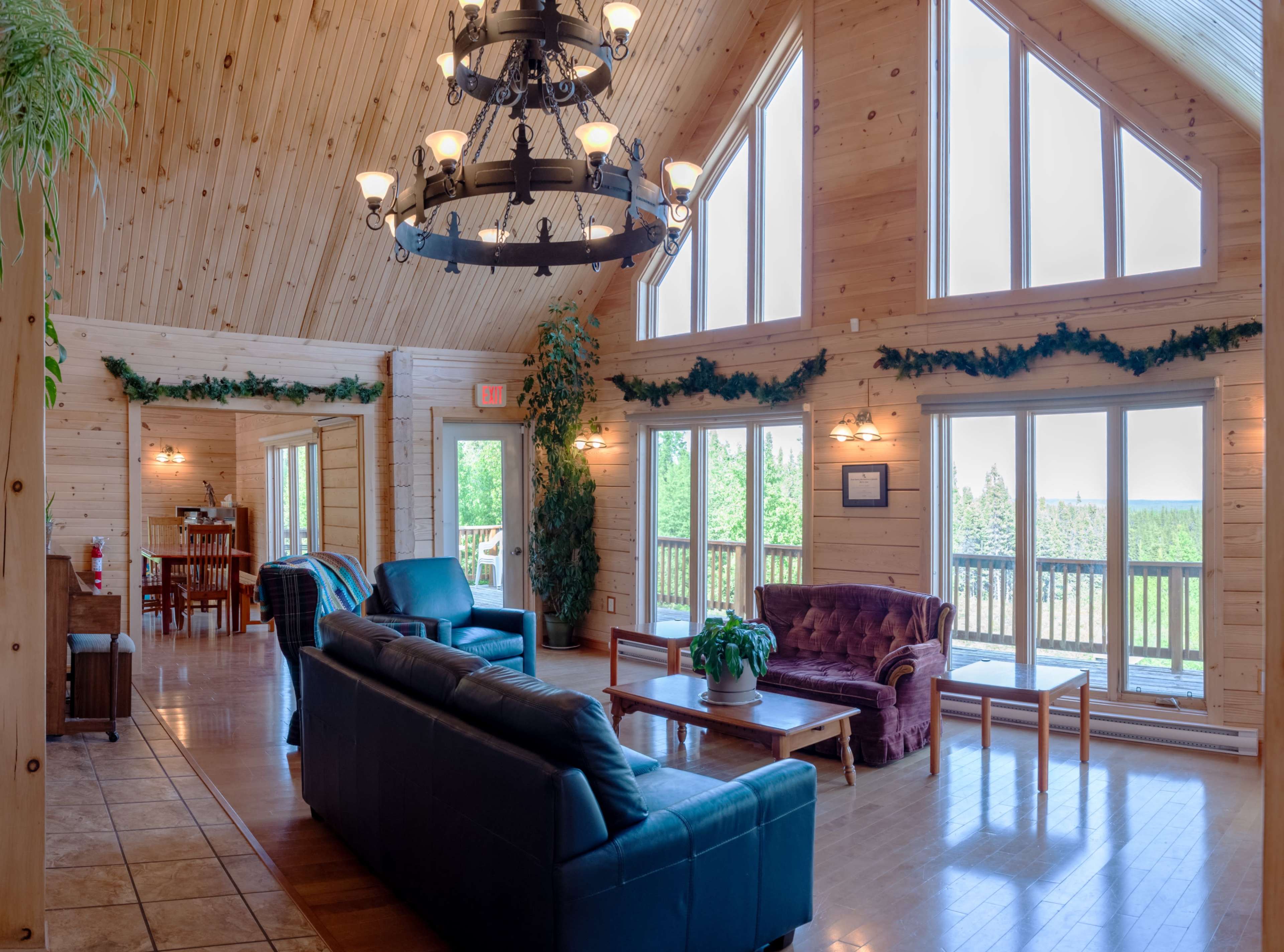 A spacious wooden interior living area with large windows, a chandelier, and comfortable seating.
