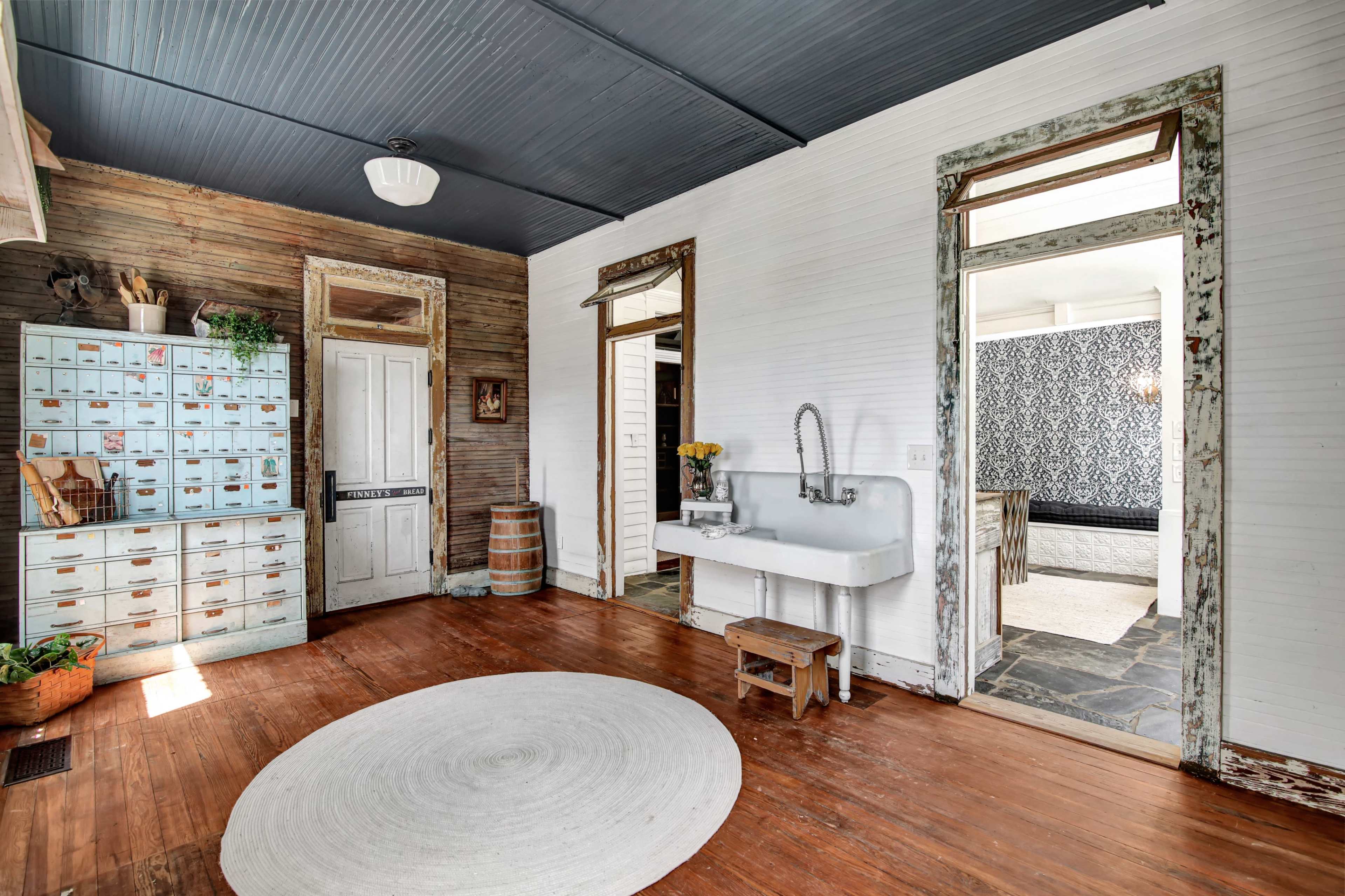 A rustic interior room with a wooden floor, a vintage sink, a wall of blue storage cabinets, and a doorway leading to another room.