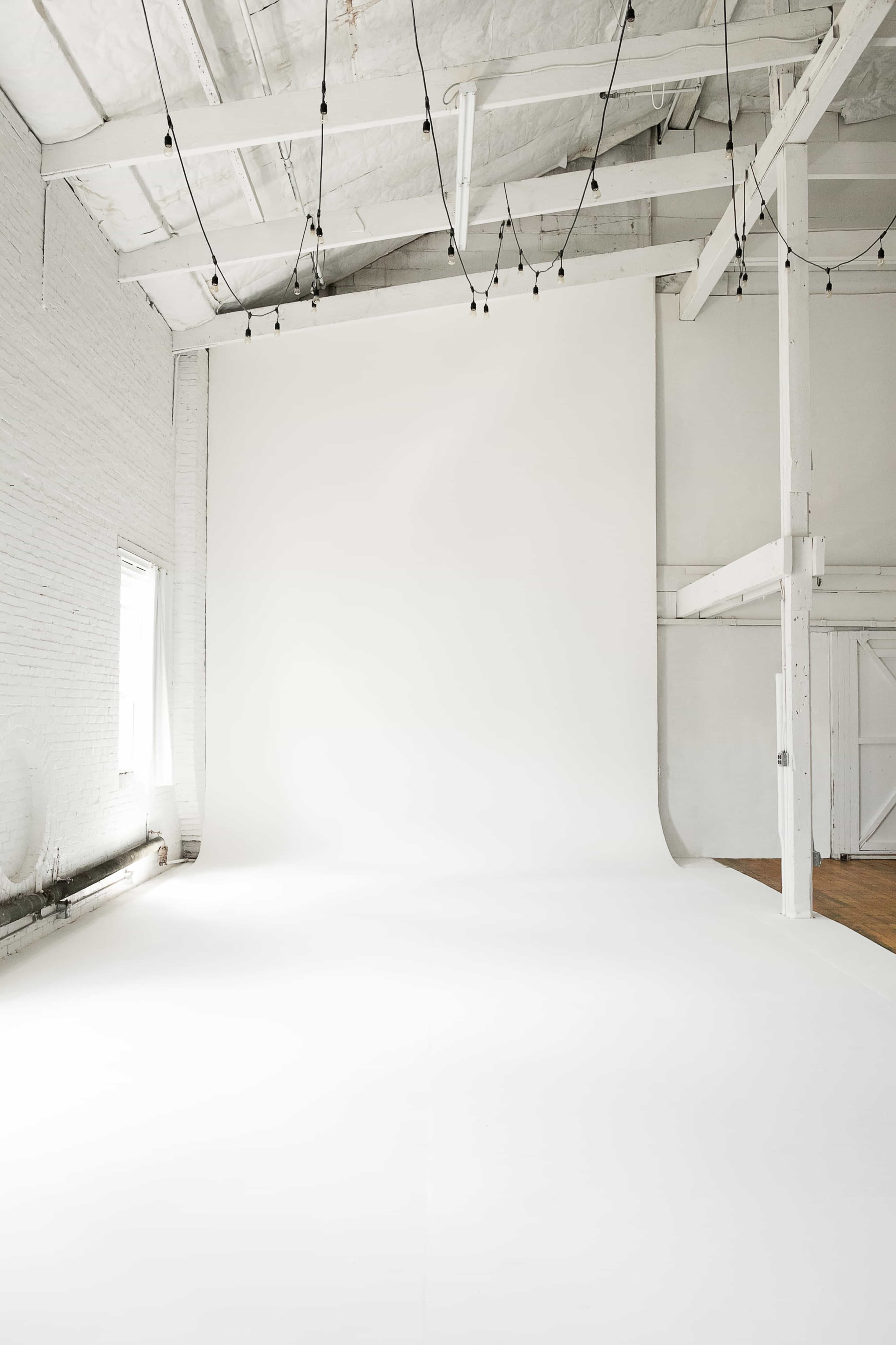 The image shows a spacious, well-lit photography studio with a large white backdrop and wooden flooring.