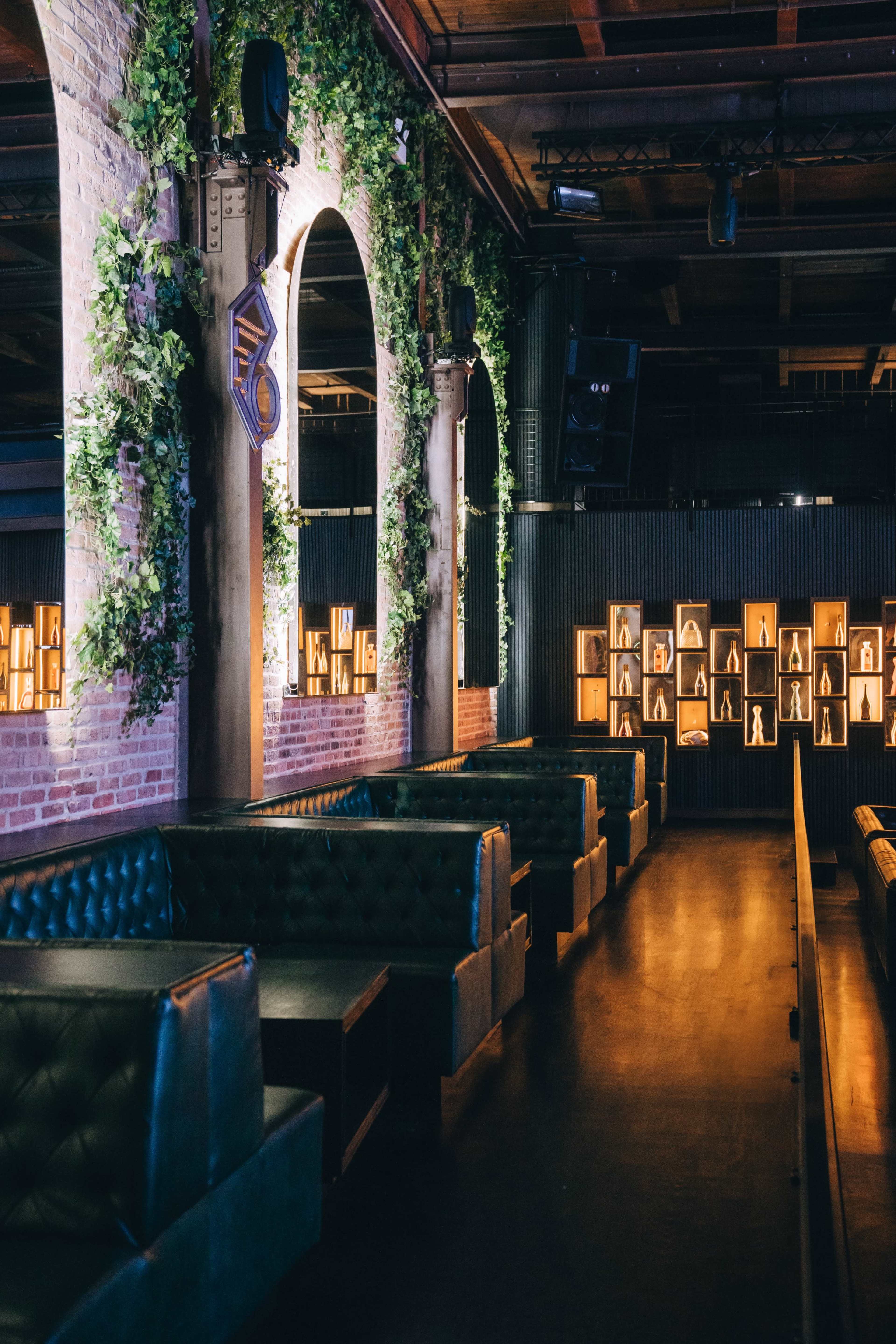The image shows a modern lounge with green plants on the walls, leather seating, and illuminated wall displays.