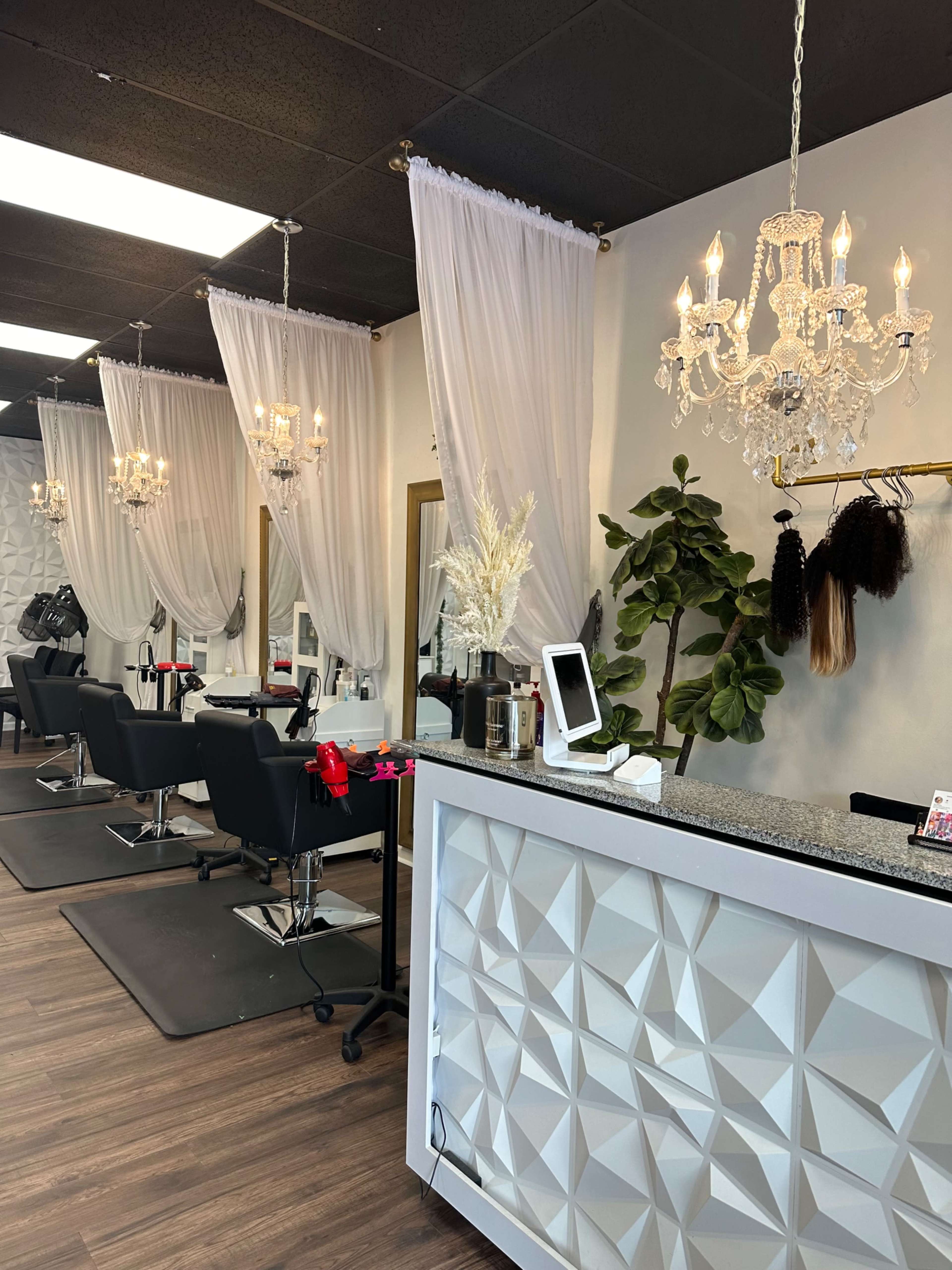 The image shows the interior of a hair salon featuring several stylist stations with black chairs, decorative curtains, and chandeliers.