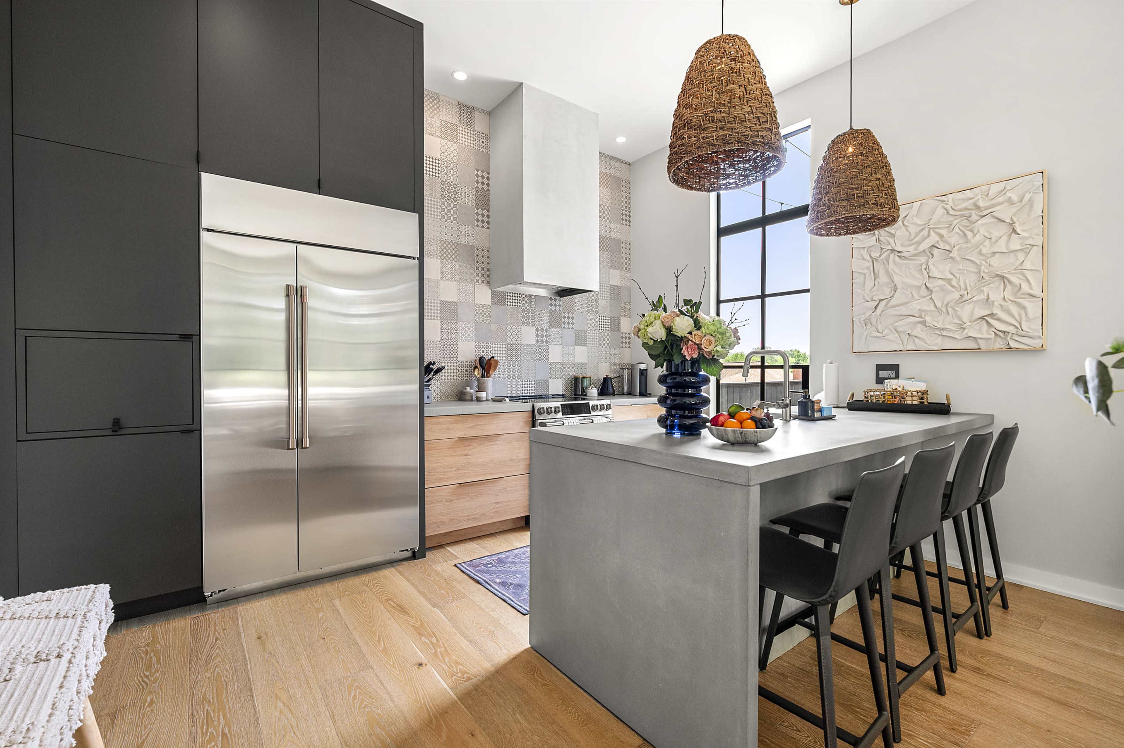 The image shows a modern kitchen featuring sleek black cabinetry, stainless steel appliances, a central island with bar stools, and pendant lighting above.