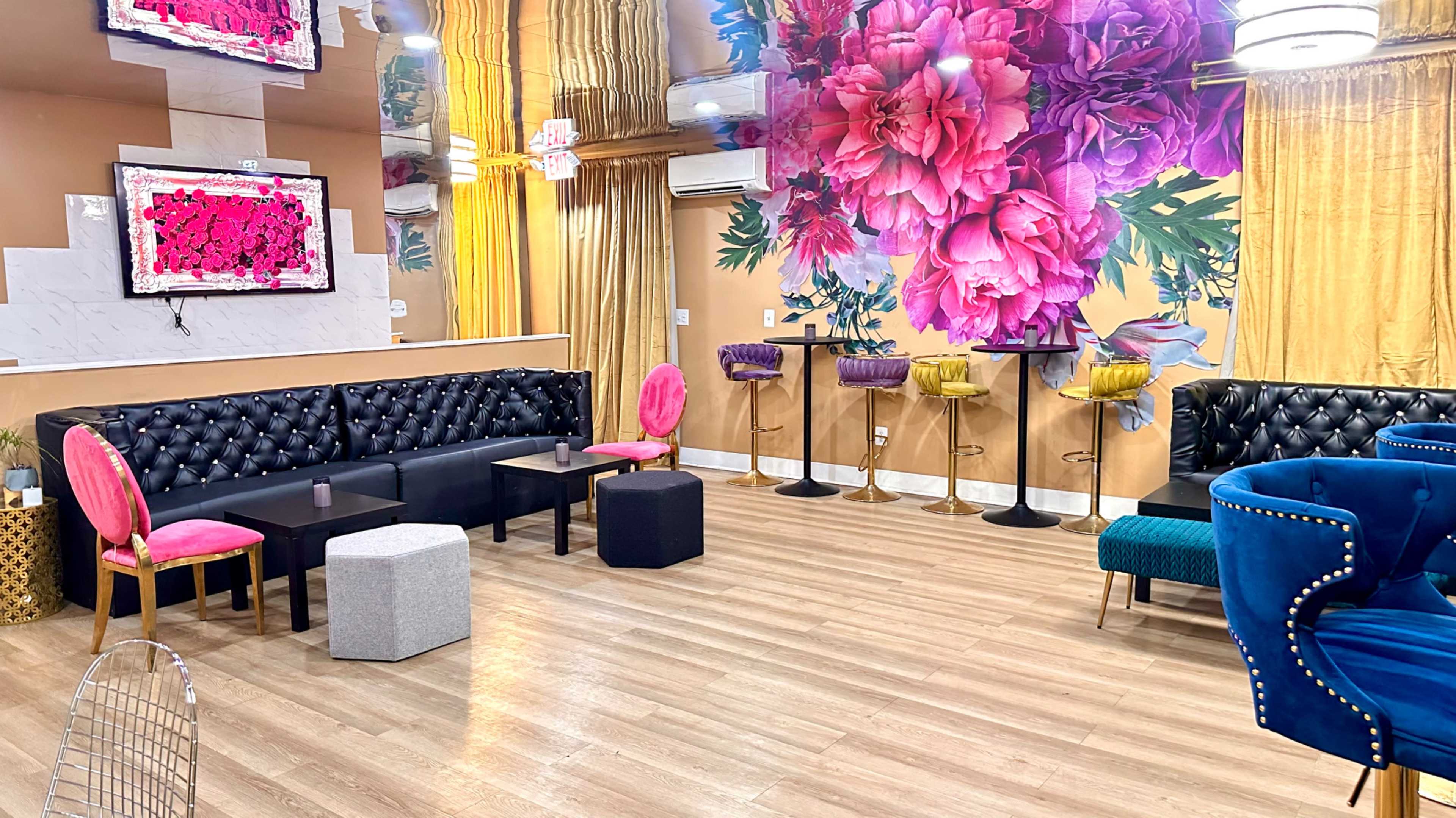 The image shows a vibrant lounge area featuring decorative floral wall art, modern seating arrangements, and a mix of colorful chairs and tables.