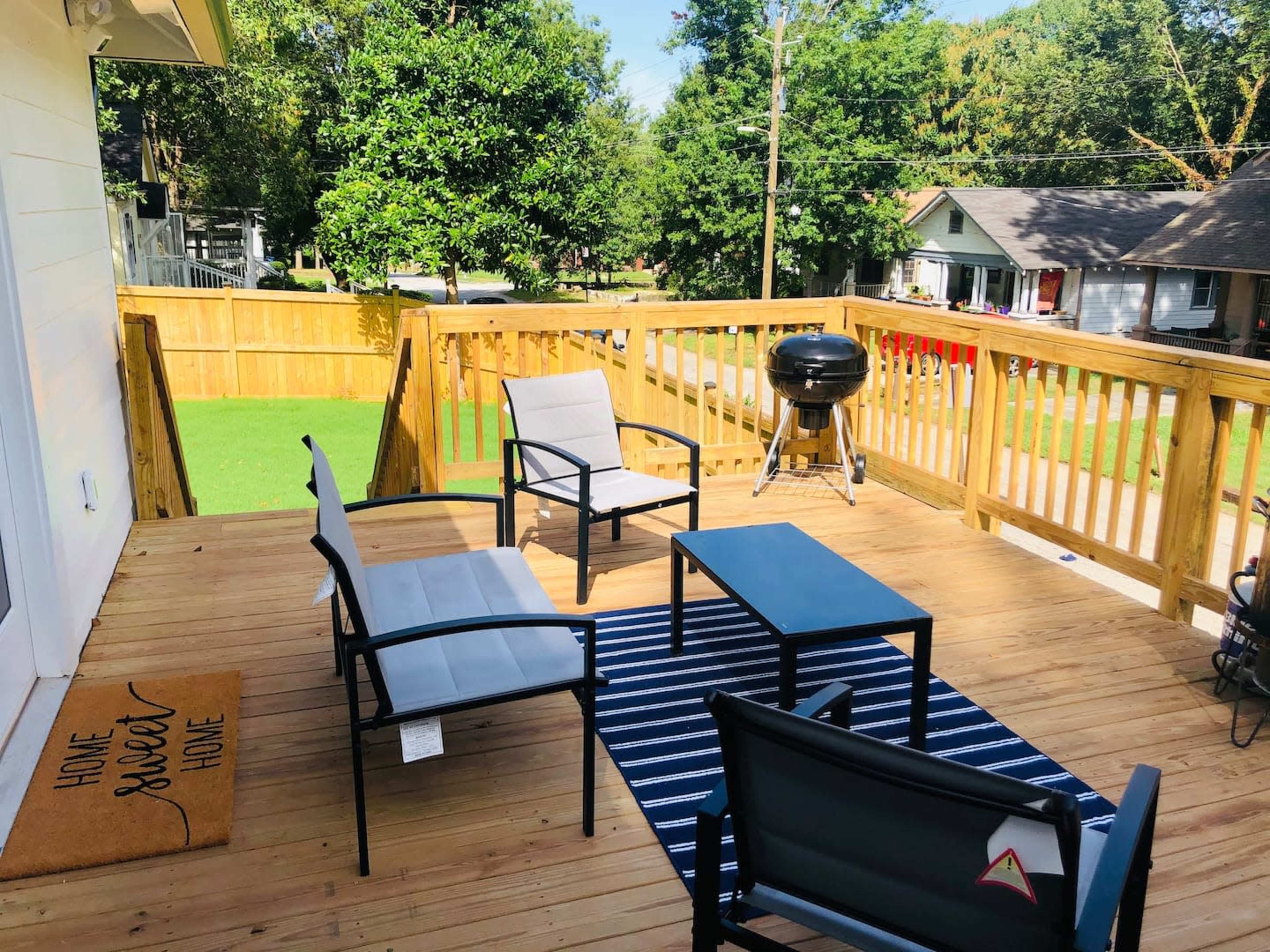 A wooden deck with four chairs, a table, a grill, and a welcome mat that reads "Home Sweet Home."