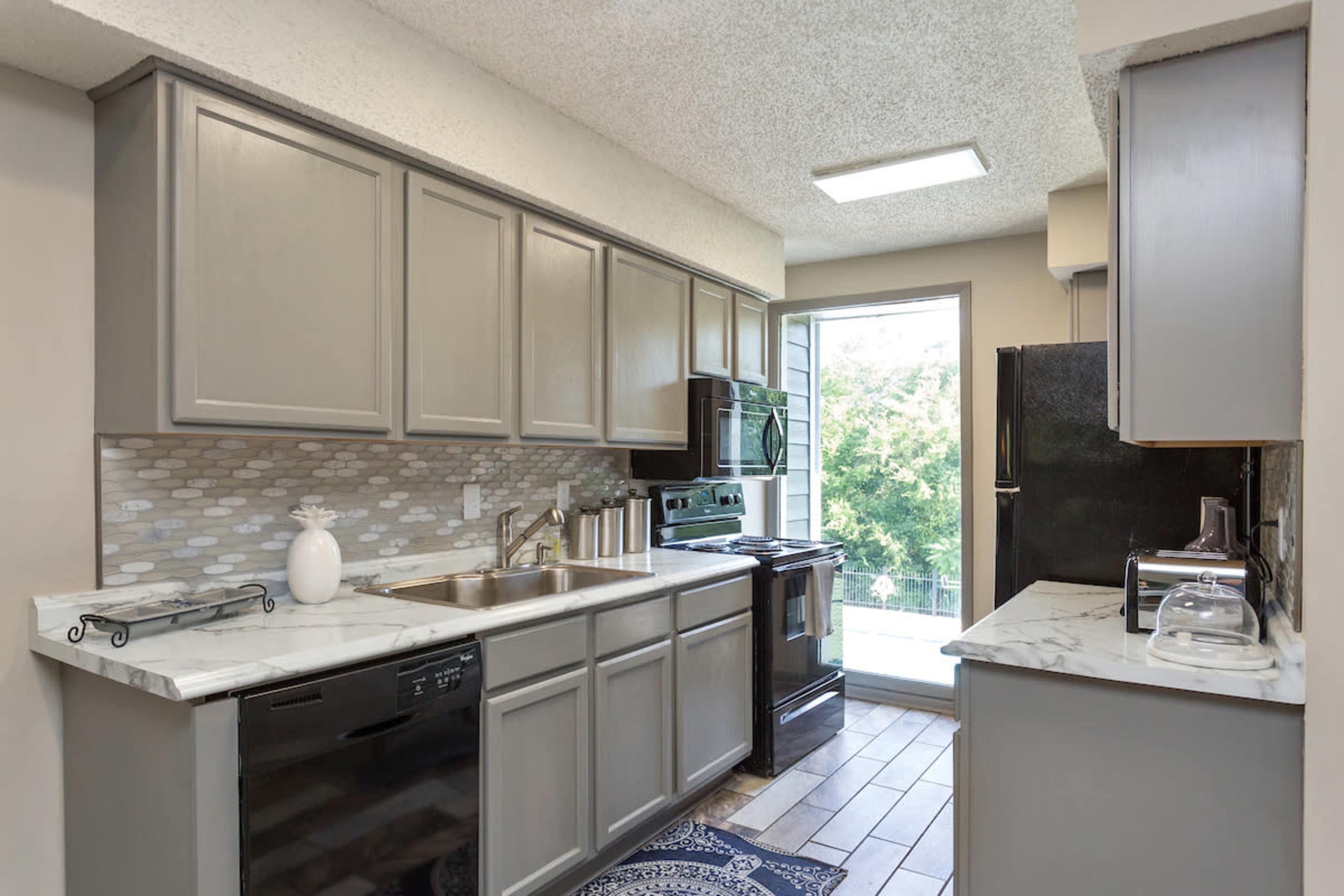 A modern kitchen featuring gray cabinets, black appliances, and a window overlooking a green landscape.