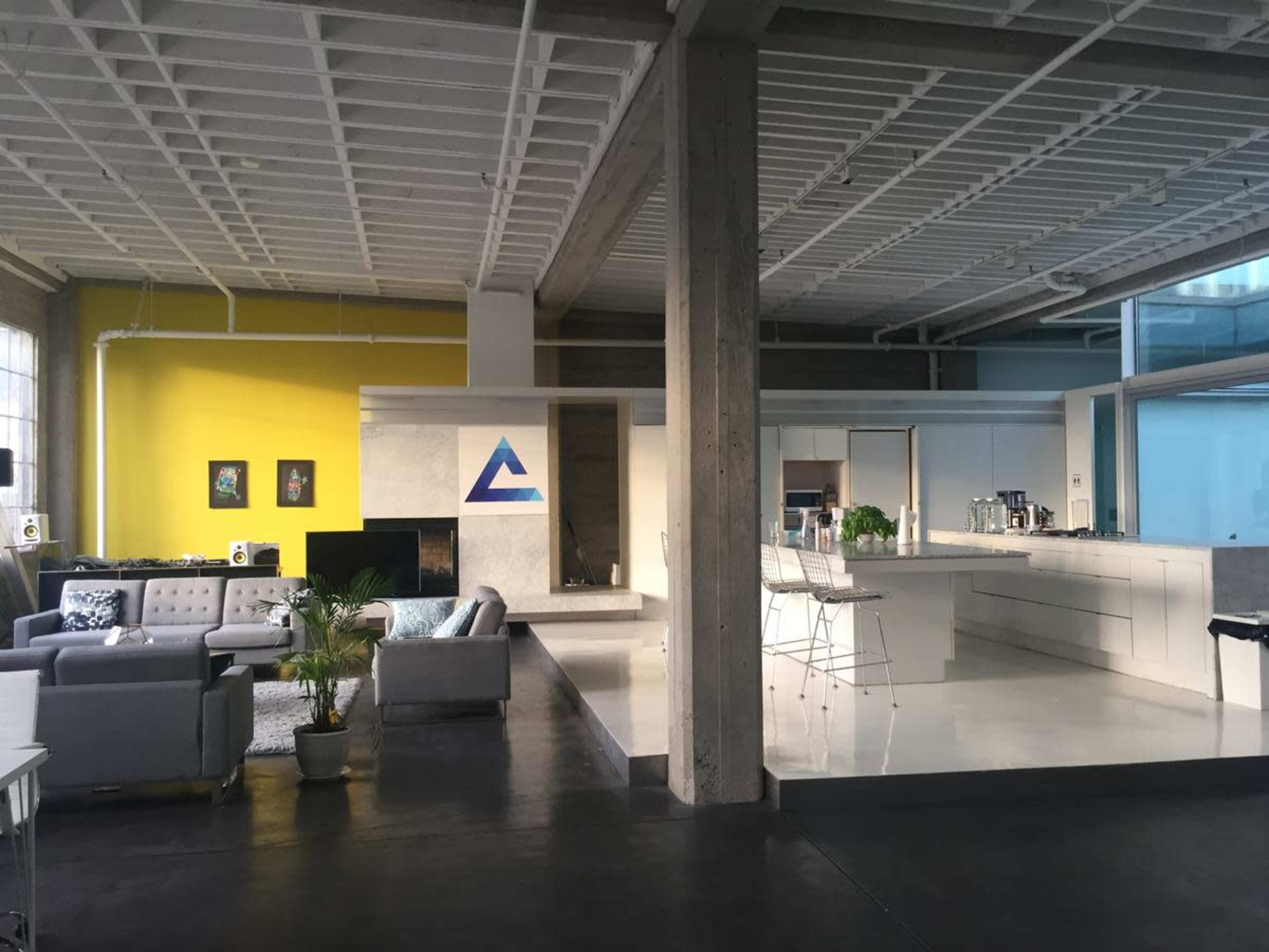 A modern, open-concept living area and kitchen with a mix of gray and yellow walls, concrete pillars, and sleek white furniture.