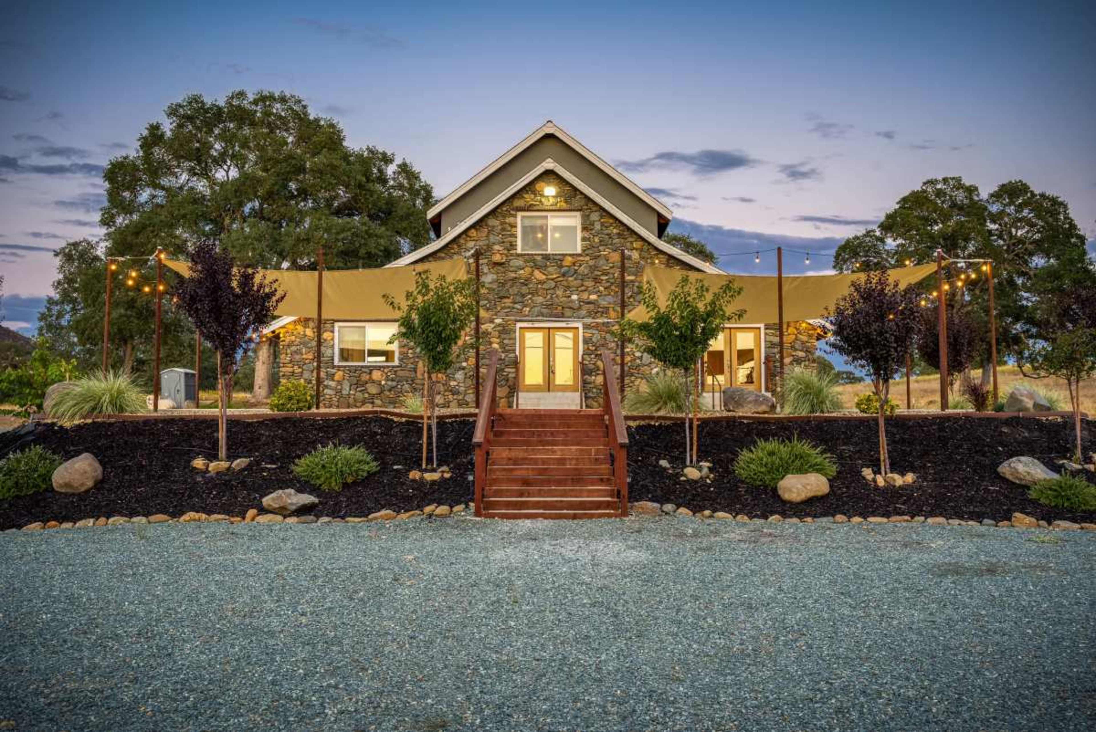 A stone house with a sloped roof, surrounded by landscaped gardens and decorative lighting.